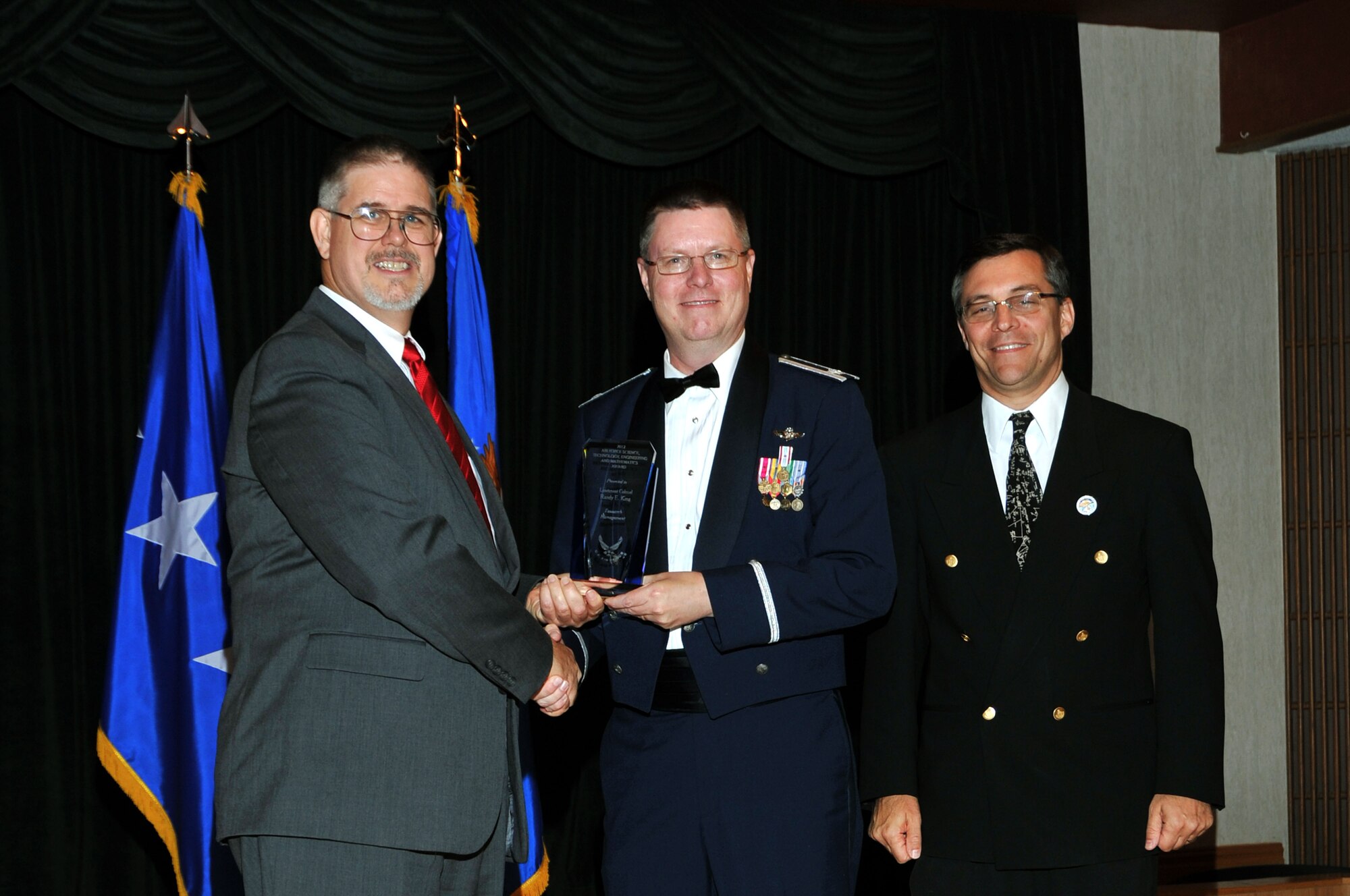 David Walker, Secretary of the Air Force Acquisitions deputy, and Mark Maybury, Science, Technology, and Engineering USAF chief scientist, present Lt. Col. Randy King, Nevada Test and Training Range support deputy director, the Air Force Science and Engineering Award Aug. 23, at Wright-Patterson Air Force Base, Ohio. King received the award for his efforts involving the Live-Virtual-Constructive Pilot Program, the first program to integrate constructive, or fully computer generated air and ground threats, into a live, dynamic air combat training mission. (Courtesy Photo)
