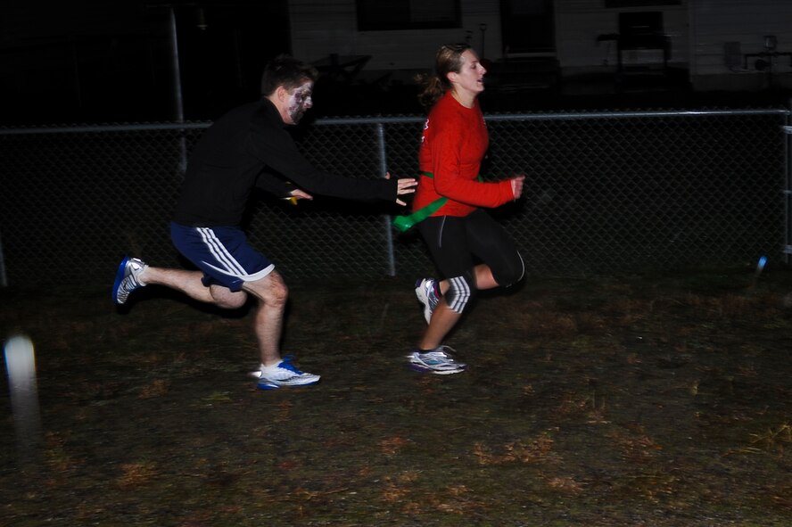 A participant in the Fairchild Airman's Running Team’s “zombie-themed” run dashes away as she is chased by Airmen in moulage makeup at Fairchild Air Force Base, Wash., Oct. 30, 2012. The event started at 6 p.m. at the Funspot and afforded medical Airmen an opportunity to practice their skills with moulage makeup which is essential for effective mass casualty exercises. The run was approximately three-to-four miles long. (U.S. Air Force photo by Senior Airman Benjamin Stratton)