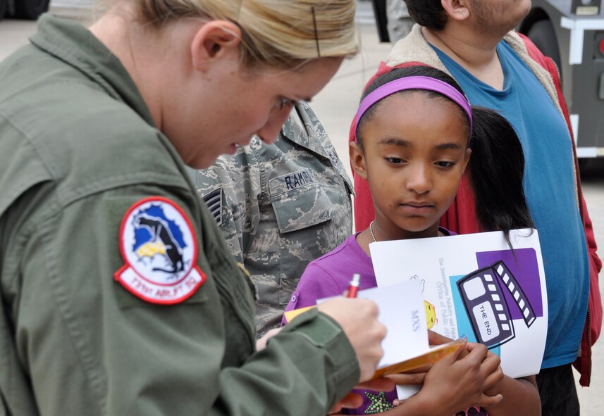 Mya, 9, watches as Air Force Reservist Senior Airman Shauna Anderson, a C-130 Hercules flight engineer, signs her Herc Adventure Tour passport Aug. 4, 2012, at Peterson Air Force Base, Colo. The Herc Adventure Tour also allowed the children of AF Reservists to experience the wing’s aeromedical evacuation mission, check out the survival gear of C-130 flight crews and sit in the pilot’s seat of a C-130 Hercules. The tour is part of the wing’s annual Family Day event. Mya is the daughter of Tech. Sgt. Rodolfo Ramirez who is assigned to the 302nd Aircraft Maintenance Squadron. (U.S. Air Force photo/Staff Sgt. Stephen J. Collier)