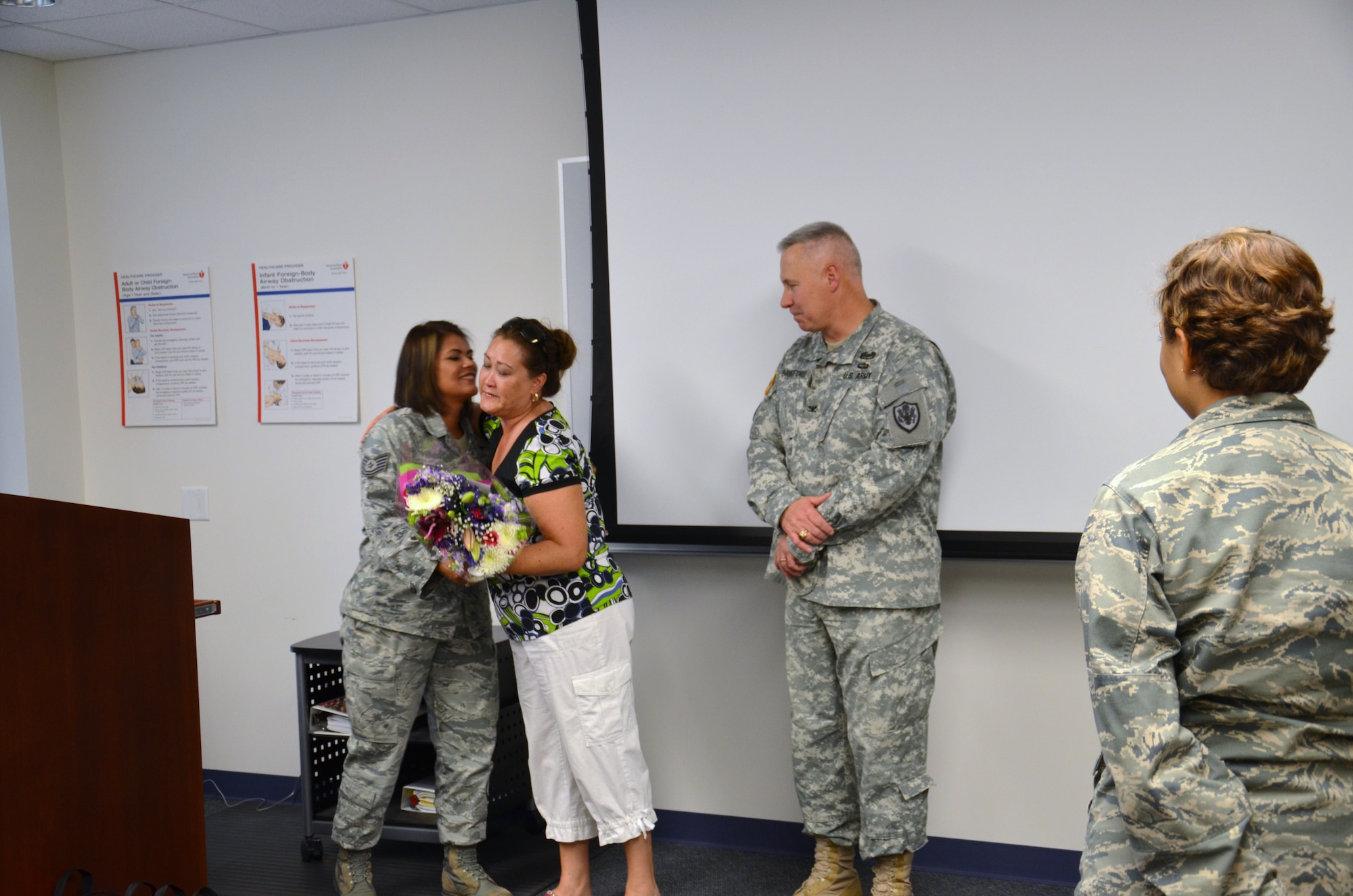 Tech Sgt. Valerie Montellano, instructor supervisor for the Air Force dental assistant program at the Medical Education and Training Campus, is surprised by Army Col. Robert Bridgford, vice commander of the 502nd Air Base Wing, while teaching a Basic Lifesaving class on Aug. 23.

Bridgford described to the class how Montellano’s training and quick thinking saved his life. He then presented Montellano with a coin while his wife, Shirley, presented her with a bouquet of flowers in appreciation for her actions that “brought him back to life”.

Bridgford collapsed while working out at the Jimmy Brought Fitness Center May 14. Montellano, along with a nurse with the AMEDDC&S Department of Nursing, immediately sprang into action and administered life support with an automated external defibrillator for approximately 15 minutes until emergency medical services arrived. According to Bridgford, if lifesaving measures were not performed within the first two minutes, he would not have survived.