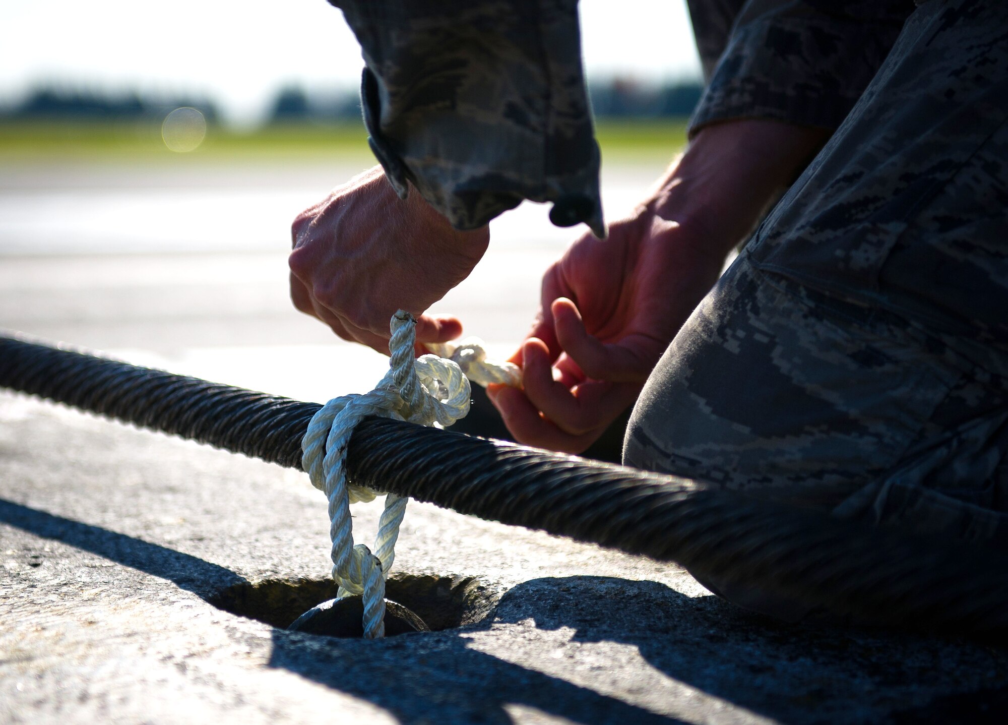 YOKOTA AIR BASE, Japan -- Airman 1st Class Johnathan Riley, 374th Civil Engineer Squadron electrical power productions technician, secures a tie-down rope on an emergency aircraft landing cable on the runway at Yokota Air Base, Japan, on Sept. 5, 2012. Due to Yokota’s shortened runway, fighter jets, such as the F-16 Fighting Falcon, would have to drop a tail hook and catch cable to stop. (U.S. Air Force photo by Staff Sgt. Chad C. Strohmeyer)