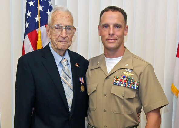 Aviation Radioman 2nd Class Harrison D. Miller receives the Distinguished Flying Cross for his heroic actions on 31 January 1944 when U.S. forces invaded Kwajalein Atoll. At 1522 local time, an OS2N-1 ?Kingfisher? observation/scout float plane from the USS New Mexico (BB-40) was hit by enemy anti-aircraft fire from Ebeye Island, an enemy float plane base at the time.  The Kingfisher suffered serious damage and was forced to make an emergency water landing in the lagoon due to high octane aviation fuel leaking into the bilges in the cockpit, filling it with fuel fumes presenting a critical fire hazard.  The pilot, Navy Lieutenant Forney O. Fuqua was mortally wounded by the enemy fire and instructed the Radioman in the rear cockpit of the Kingfisher, Harrison Miller, to bail out.  Miller elected to stay with the plane and to attempt a water landing himself from the rear cockpit.  With no prior flying experience, no flight instruments and only an emergency control stick in the rear cockpit, he successfully made a water landing from the back seat of the Kingfisher.  After landing, Miller got out of the rear cockpit onto the wing and made his way to the front cockpit and turned off the Kingfisher?s engine and started to unbuckle the pilot?s parachute and harness; but before he could get him unbuckled, the plane capsized due to the loss of the outboard pontoons during the landing.  Miller made numerous attempts to rescue the pilot and remove him from the cockpit, diving under the gasoline covered waters but was unsuccessful.