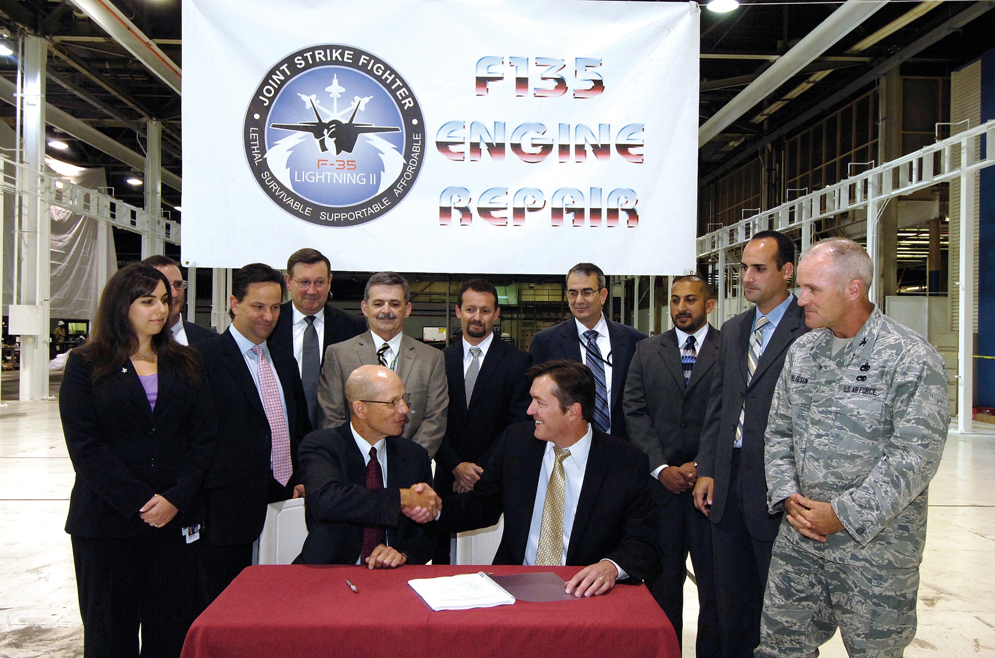A signature and congratulatory handshake make it official Aug. 30 when Oklahoma City Air Logistics Complex Vice Director Kevin O’Connor, seated right, and Pratt & Whitney President of Military Aftermarket Services Douglas Cleary, signed an implementation agreement for F135 engine work. The F135 engine, which powers the F-35 Joint Strike Fighter aircraft, will be jointly maintained in the Bldg. 3001 area behind the signers, which is currently being transformed into a dedicated repair area for the engine. (Air Force photo by Margo Wright)