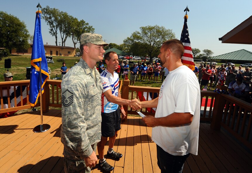 U.S. Air Force Master Sgt. Dennis Carr along with Rick Sanders of the Offutt Advisory Council present a check to Casey Miller, the founder of the Long Road Home project at a formal ceremony held at the Base Lake on Offutt Air Force Base, Neb., Aug. 30.  The additional money will aid in the five cyclists riding from Tacoma Wash. to Washington D.C. in an effort to raise money and awareness concerning veterans’ affairs.  (U.S. Air Force photo by Josh Plueger/Released).