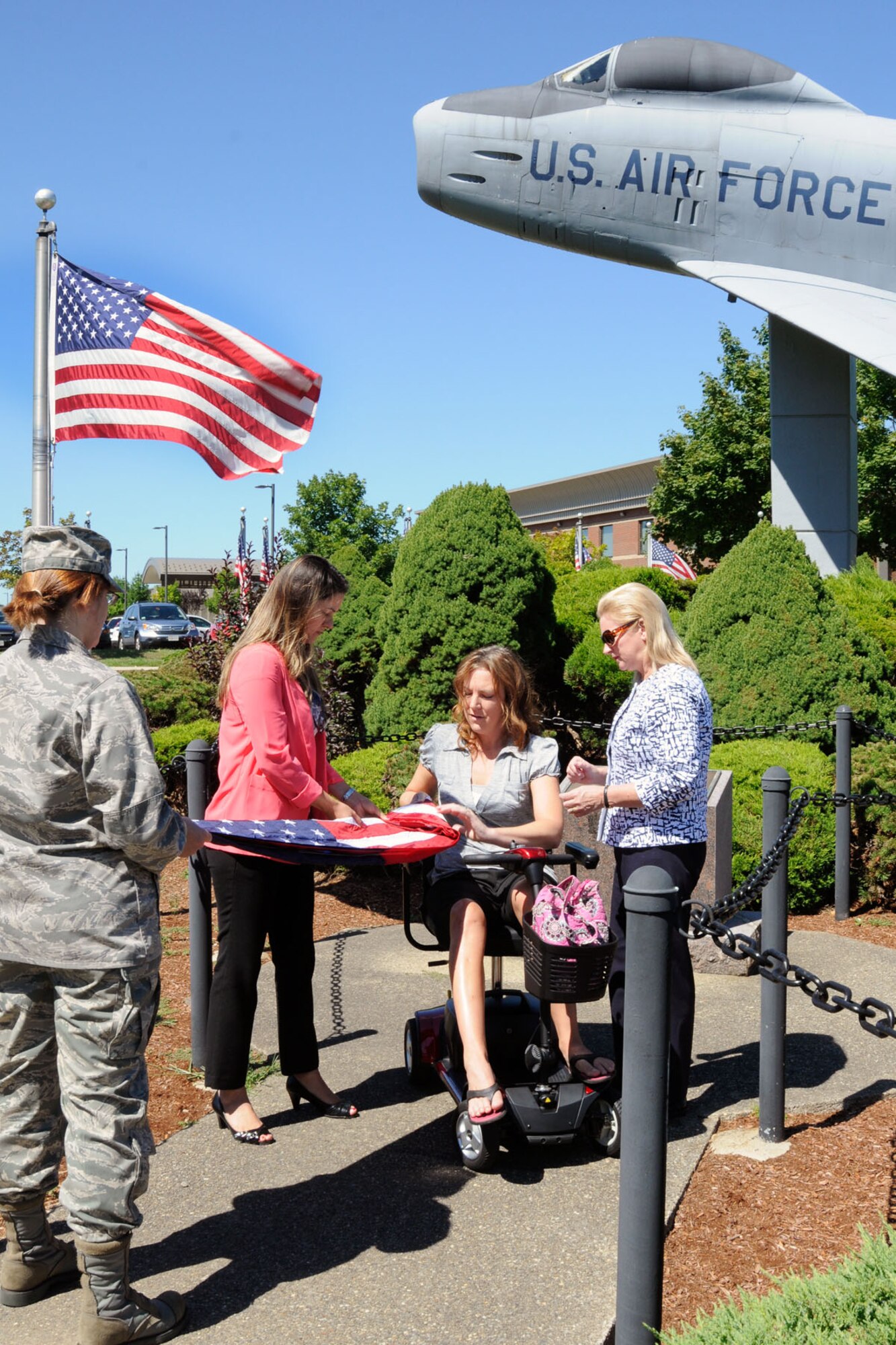 HANSCOM AIR FORCE BASE, Mass. - Capt. Alexis Presti-Simpson (left), Ferenda Presti and Mary Presti help fold an American flag with Kelsey O’Connor in front of the F-86 static display Aug. 29. O’Connor, a Navy veteran, accepted a power scooter that was donated to the Wounded Warrior project by the Presti’s from Boston Walk-In Bath and Stairlift company. (U.S. Air Force photo by Linda LaBonte Britt)
