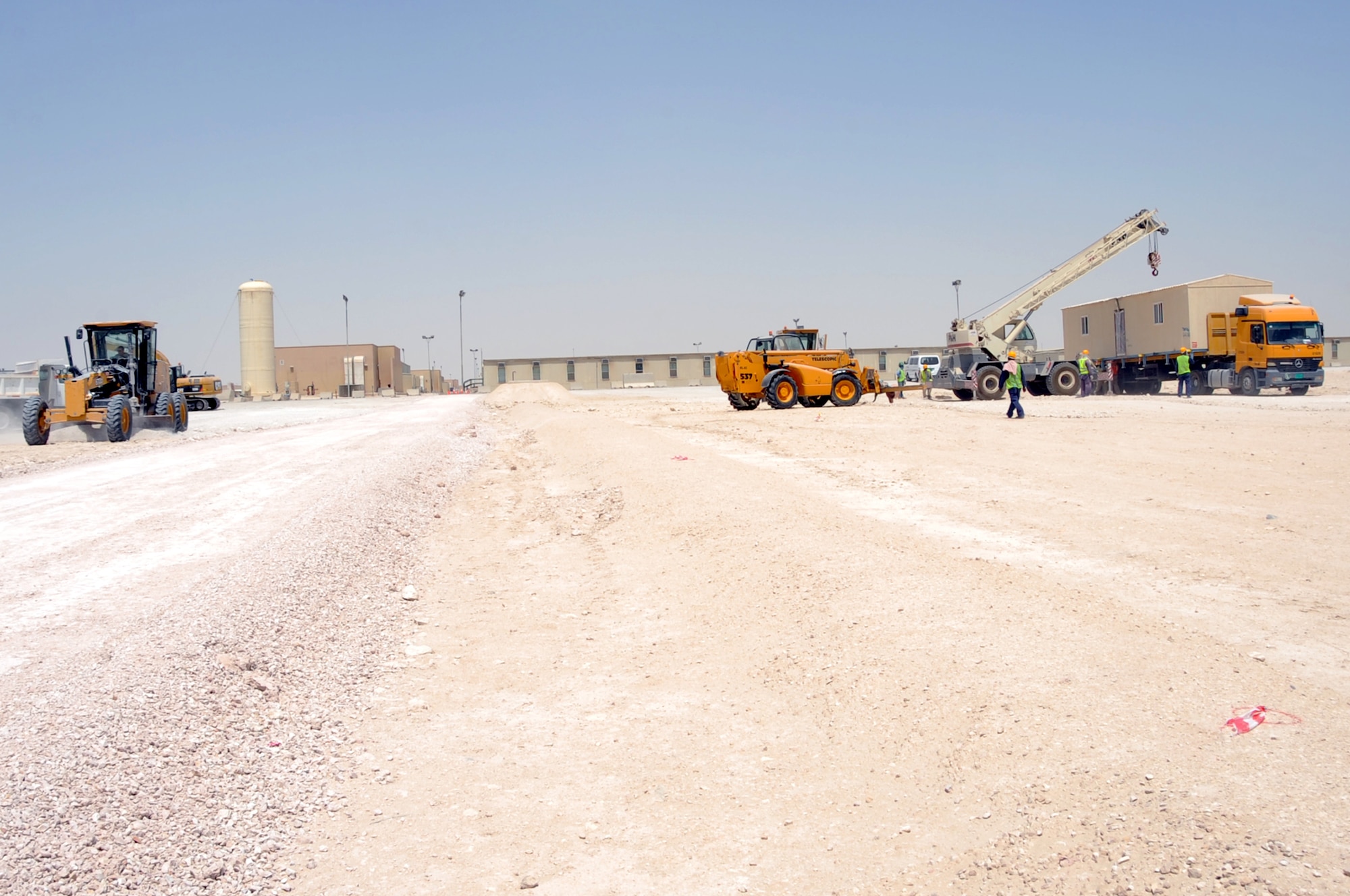 U.S. Air Force Tech. Sgt. Matthew Bell (left), 379th Expeditionary Civil Engineer Squadron pavement and equipment craftsman, finishes grading the pathway that will connect the Blatchford Preston Complex and the Coalition Compound while civilian workers prepare to move a mobile storage facility in Southwest Asia, September 4, 2012. This is the start of the CC Billet Refresh, a construction project for 20 new two-story buildings with 64 rooms per building and indoor latrines to serve as the future of CC lodging. (U.S. Air Force photo/Staff Sgt. Sheila deVera)
