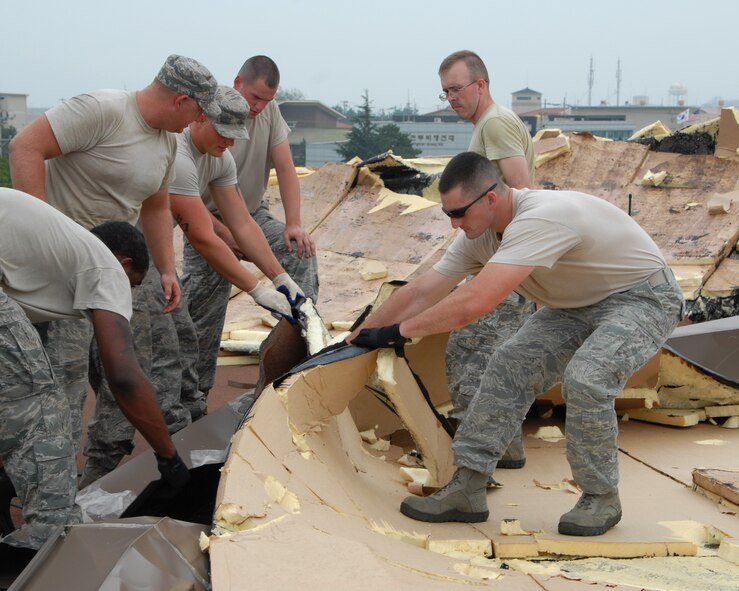 Members of the 8th Civil Engineer Squadron Fire Department help remove damaged shingles from the roof of a building after Typhoon Bolaven passed through Kunsan Air Base, Republic of Korea, Aug. 29, 2012. The Airmen’s quick repair job helped prevent further damage by rain to the building. (U.S. Air Force photo/Senior Airman Marcus Morris)