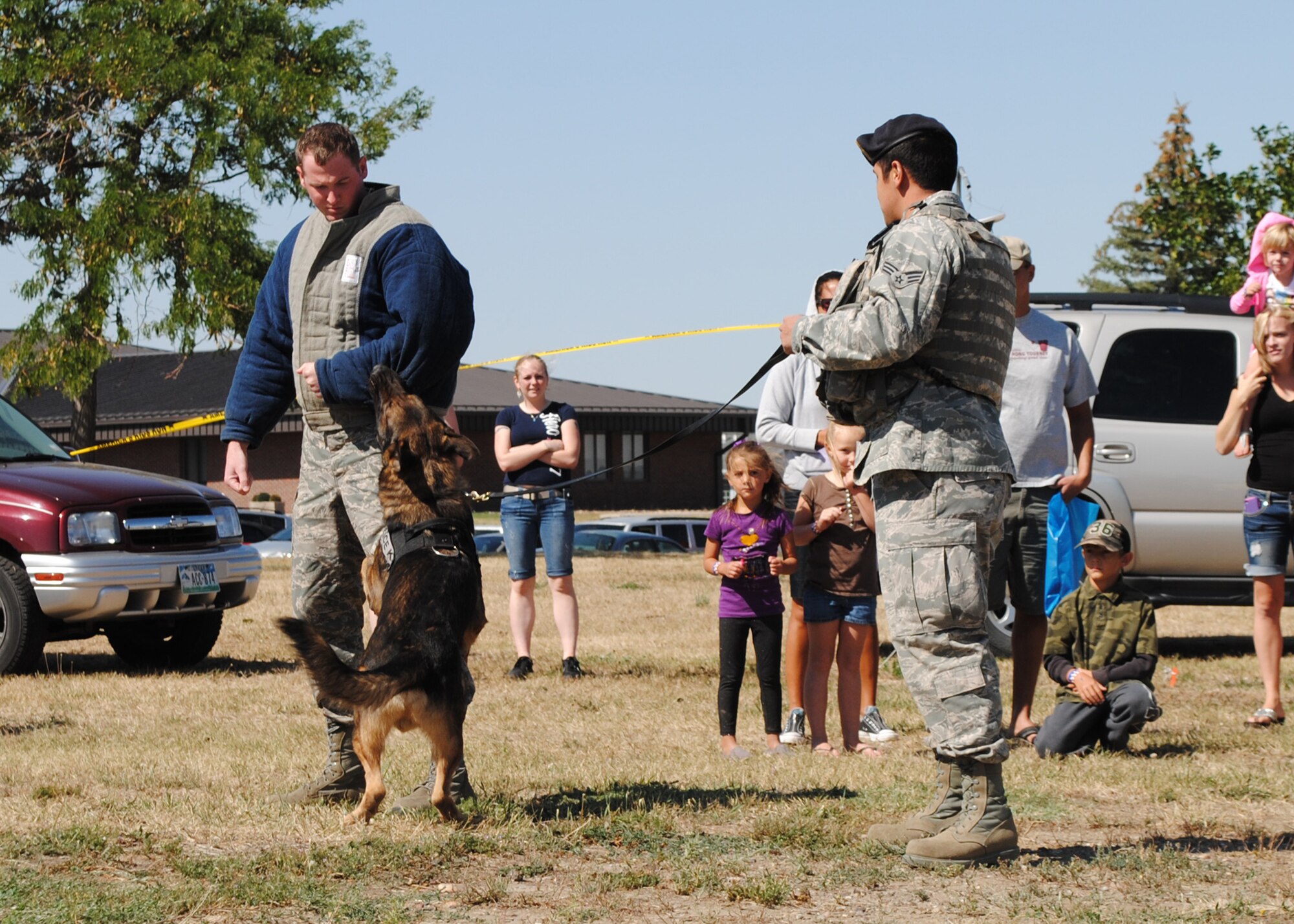 Senior Airman Bradley Stickle, 341st Security Forces Squadron member, left, and Senior Airman Antonio Padilla, 341st SFS military working dog handler, demonstrate how to apprehend a subject during a controlled aggression demonstration with a military working dog.  This demonstration was one of many opportunities for children to see what their parents do; others included a children’s deployment line as well as static displays of military vehicles and equipment.  (U.S. Air Force photo/Airman 1st Class Katrina Heikkinen)