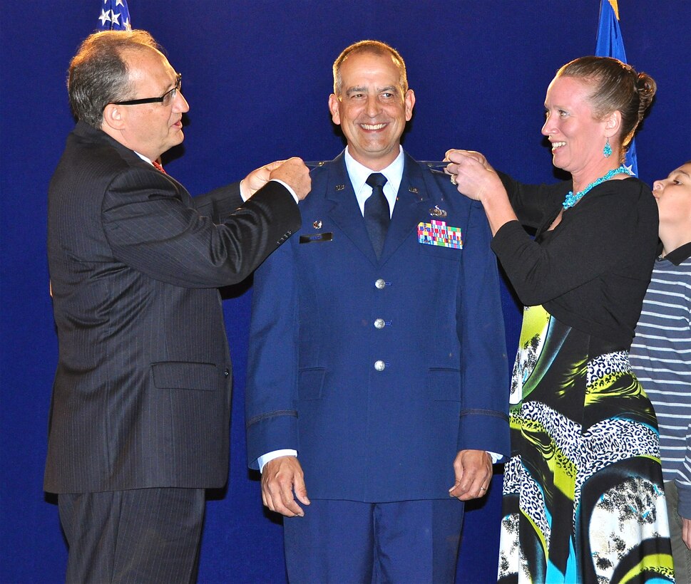Mr. Renne, the director of Public Affairs and Communications and Col. Mench's wife pin on the new rank of Lt. Colonel.