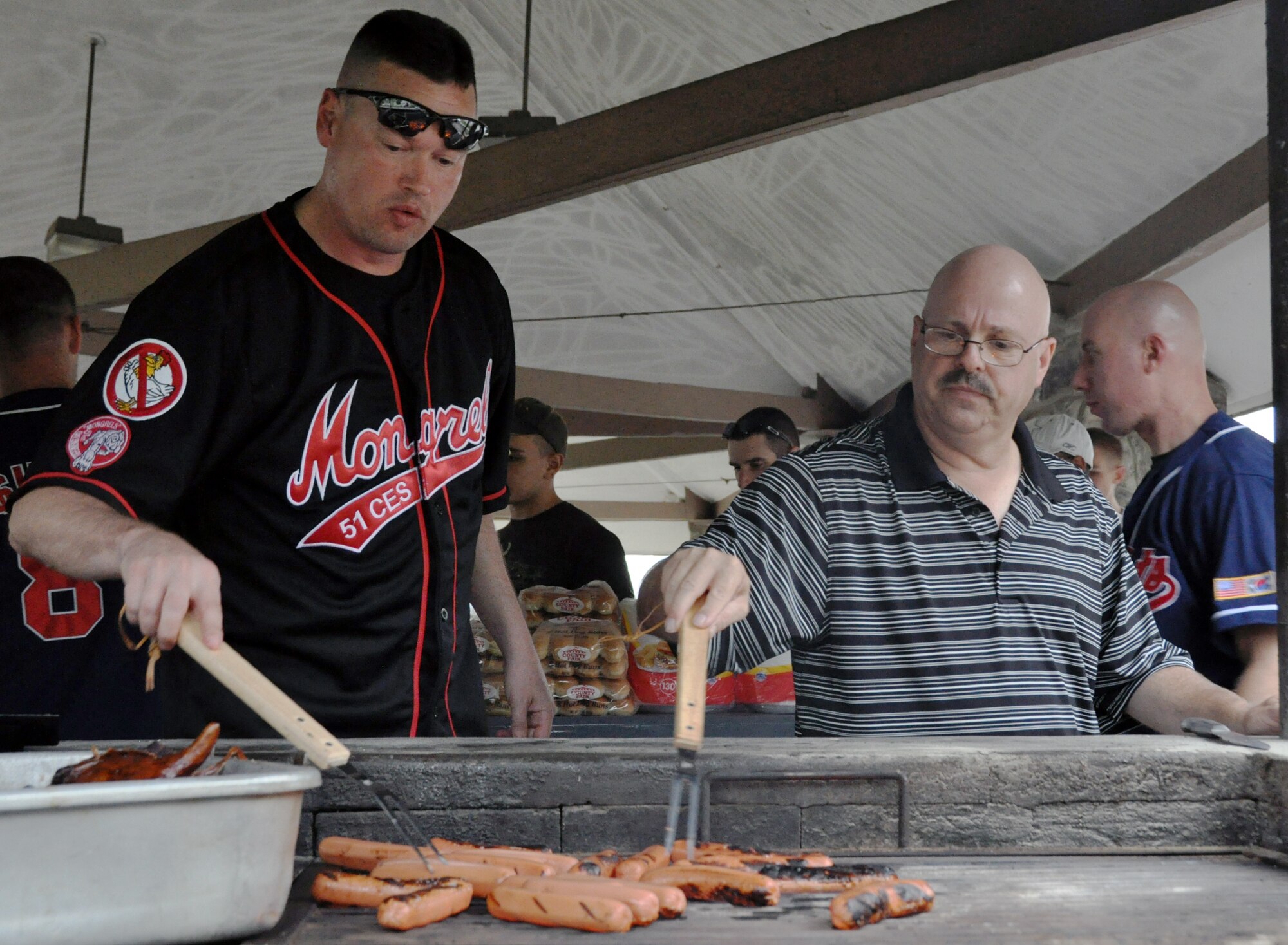 Senior Master Sgt. Jack Fox (left), and Master Sgt. Michael Grant flip hot dogs during a first sergeant pig roast for single and unaccompanied Airmen at Osan Air Base, Republic of Korea, Sept. 7, 2012. Airmen had a chance to eat a free meal and talk with their fellow Airmen at the first-time event. Fox is the 51st Civil Engineer Squadron first sergeant and Grant is the 51st Security Forces Squadron assistant first sergeant. (U.S. Air Force photo/Senior Airman Michael Battles)