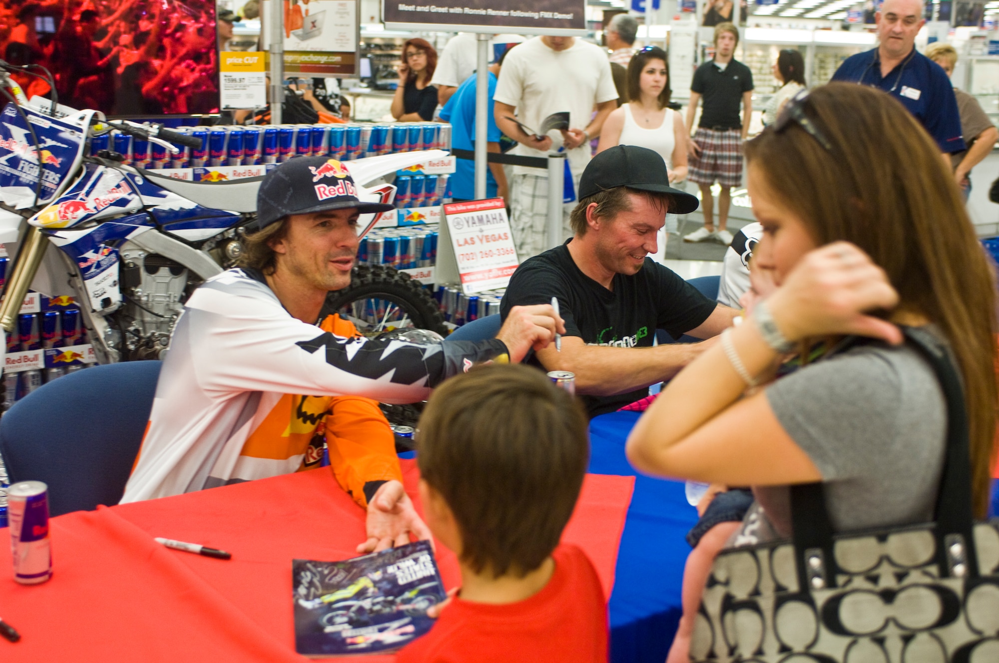 Rodney Renner and Ted Culbertson, Red Bull Jams motocross rider, sign booklets at a meet and greet Sept. 8, 2012, at The Exchange here. The signing took place after the Red Bull Jams X-Fighters put on a small demonstration for Airmen and their families here. (U.S. Air Force photo by Senior Airman Jack Sanders)