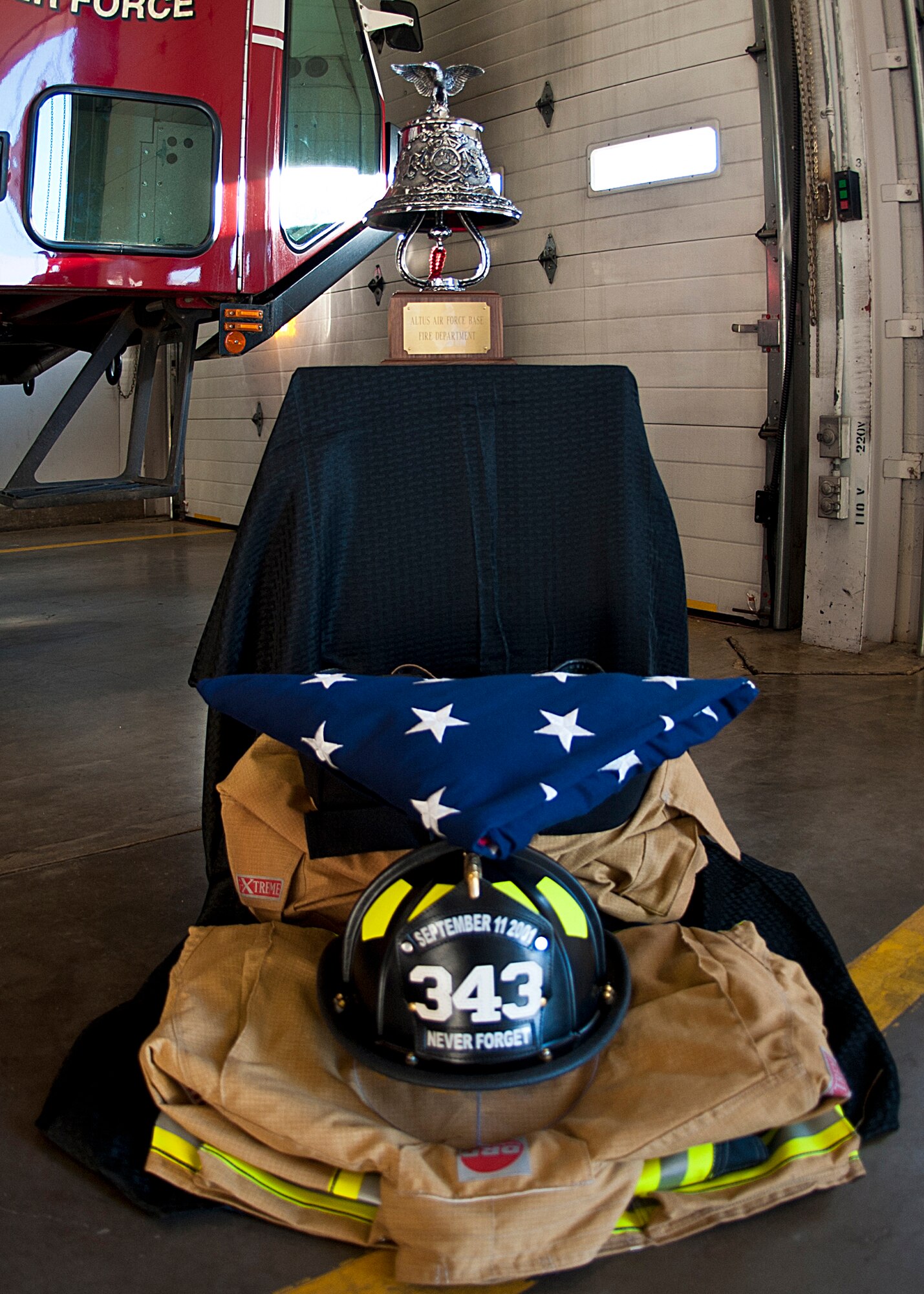ALTUS AIR FORCE BASE, Okla. – A ceremonial bell, folded flag, firefighter uniform, and memorial helmet are displayed at the base Fire Department for The Last Alarm Ceremony, Sept. 11, 2012. The ceremony was held to honor the 343 firefighters who made the ultimate sacrifice Sept. 11, 2001.  During the ceremony the bell was rung in a series of five rings, four times, to honor the 343 firefighters who gave their lives. (U.S. Air Force photo by Senior Airman Kenneth W. Norman / Released / 97th Air Mobility Wing Public Affairs)