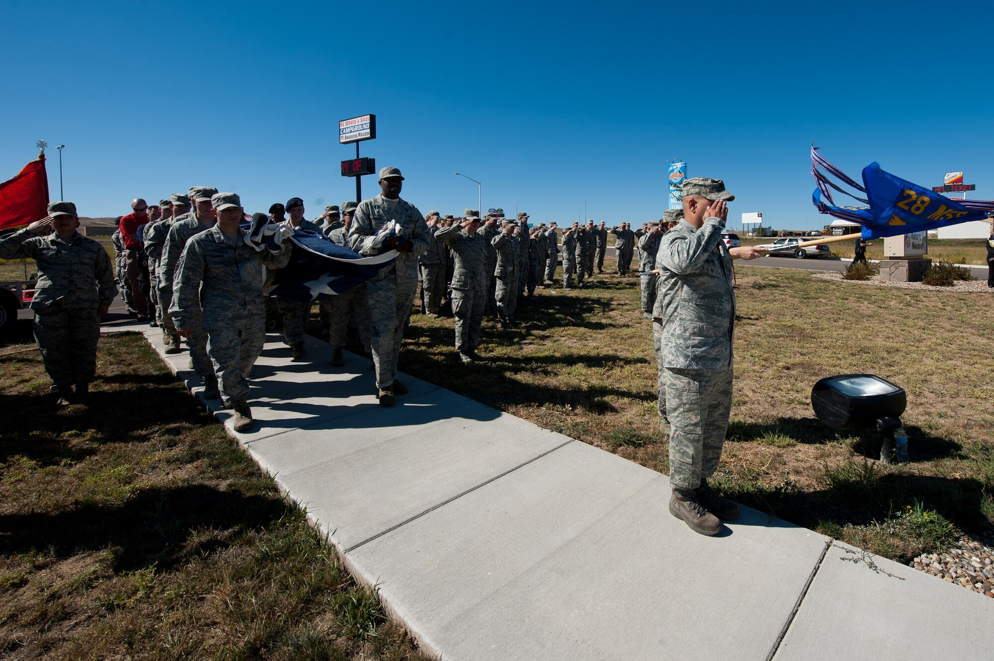 Airmen of the 28th Security Forces Squadron carry a large American flag while comrades from other units render proper customs during a flag raising ceremony as part of the 9/11 Remembrance Ruck March on Ellsworth Air Force Base, S.D., Sept. 8, 2012. Nearly 150 Ellsworth Airmen, family members and friends teamed up with area police officers, firefighters and other first responders for the 11-mile rucksack march to commemorate the 11th anniversary of 9/11. (U.S. Air Force photo by Airman 1st Class Kate Thornton-Maurer)