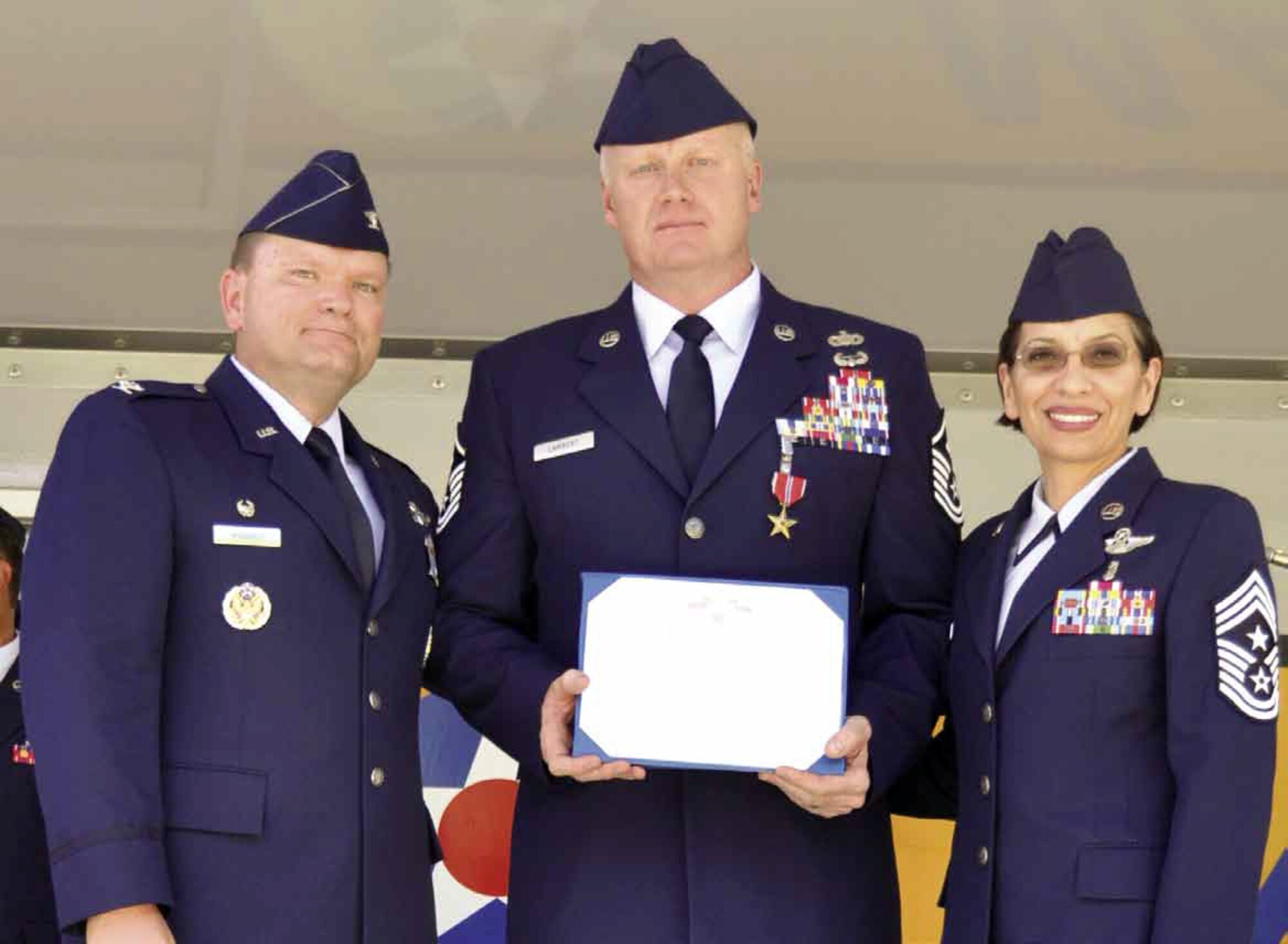 Pictured from left to right are Col. Samuel C. Mahaney, 452d AMW commander, Master Sgt. Jim Lambert, 729th AS and Chief Master Sgt. Ericka Kelly, 452 AMW command chief. Lambert was awarded the Bronze Star medal with Valor for heroism while engaged in ground operations against the enemy at Bagram Air Field, Afghanistan, Aug. 20, 2011. He is recognized particularly for his response to a fire that was caused by attacking insurgents. As a civilian firefighter, he drew upon his expertise and proposed a superior course of action to the on-scene commander. He voluntarily entered into a burning compound to distribute and employ heavy equipment resources to contain the blaze. While doing so, he spotted a crate of grenades that were about to be engulfed by flames and removed them before their certain explosion — ultimately ensuring the safety of more than 50 emergency responders that would have been in that area. His  heroic actions and unselfish dedication to duty reflected great credit upon himself and the U.S. Air Force. (U.S. Air Force photo by Senior Airman Isis Ponce)