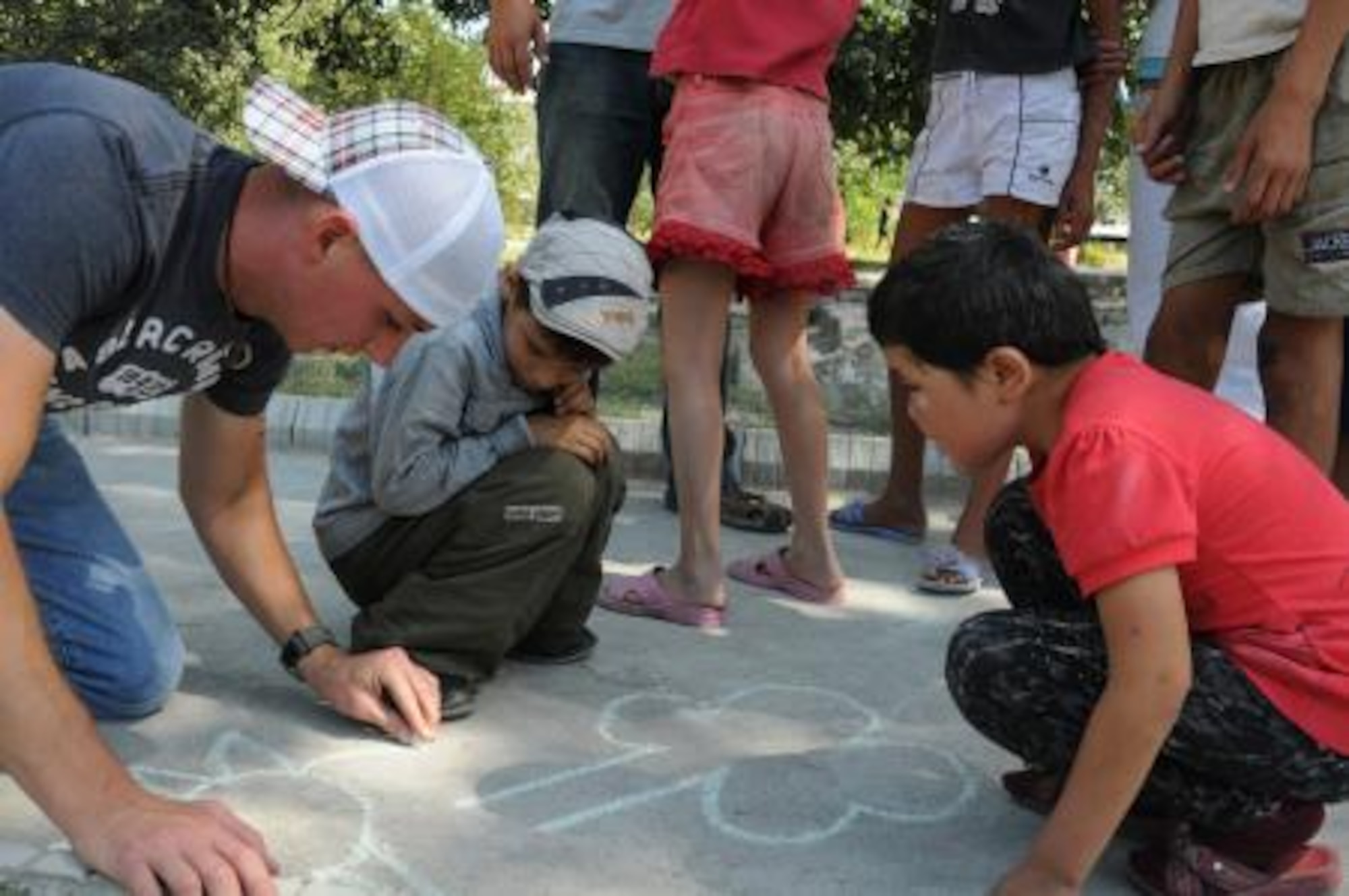 Staff Sgt. Calin Cronin draws a picture on the sidewalk with Igor and Katya during visit to Red River Orphanage, Krasnaya Rechka, Kyrgyzstan, Sept. 1, 2012. Cronin is a 376th Expeditionary ESFS, NCOIC physical security at the Transit Center at Manas and volunteers during his off-duty time to the 376 ESFS "Cops for Kids" program. The outreach program helps to deliver groceries and school supplies to children like Igor and Katya who reside at the orphanage. Cronin is a native of Rochester, Ill., and is deployed from Scott Air Force Base, Ill. (U.S. Air Force photo/Staff Sgt. Matthew Benedetti)