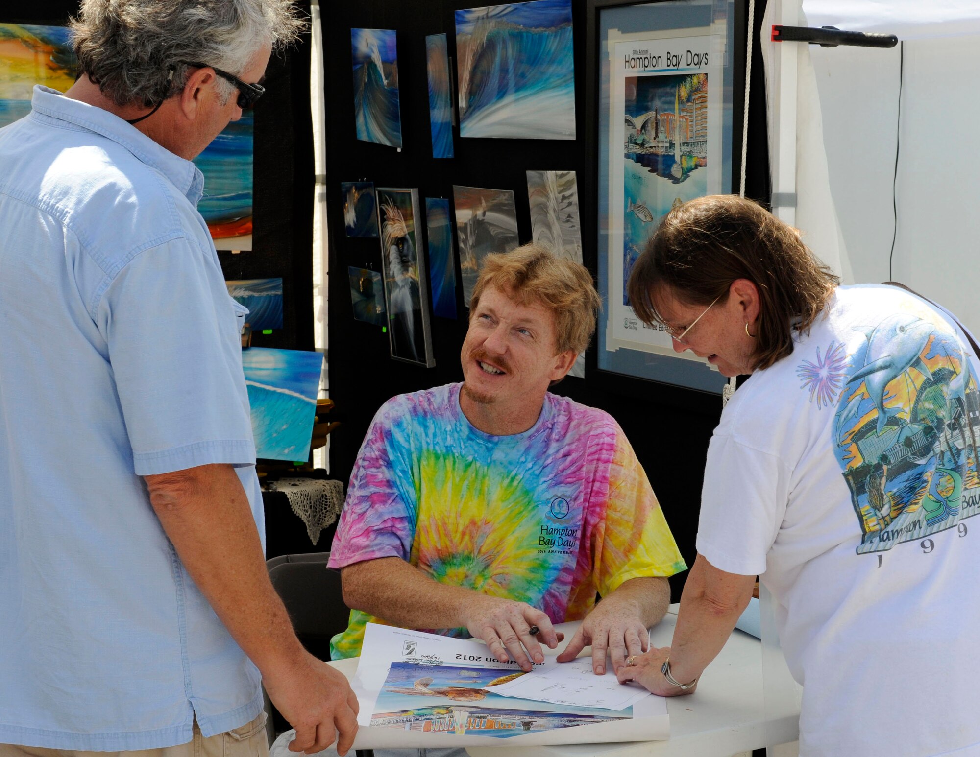 Bryan Lopatic, a U.S. Air Force supervisory illustrator and Air Combat Command Multimedia Center section chief, autographs a copy of his winning poster for festival patrons Ralph and Tina Roberts at the 30th Annual Hampton Bay Days festival in Hampton, Va., Sept. 8, 2012. As the festival’s winner, Lopatic was awarded free booth space to sell his artwork and sign limited edition copies of the poster. (U.S. Air Force photo by Staff Sgt. Krystie Martinez/Released)
