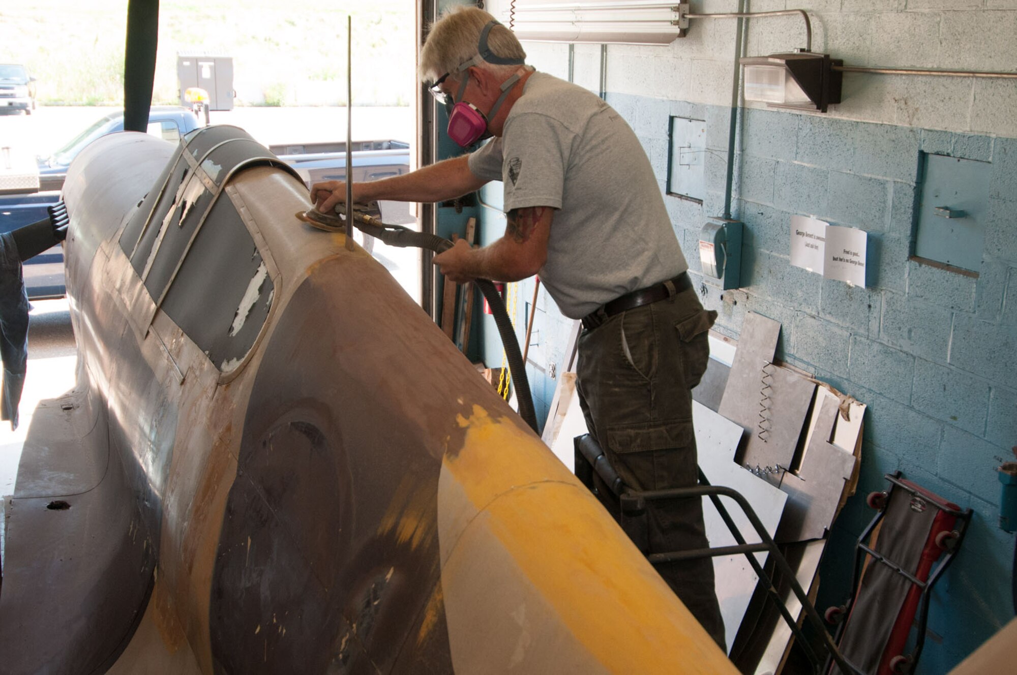HANSCOM AIR FORCE BASE, Mass. - Fredrick Smith sands the top of the P-40 in the motor pool bay on Aug. 30. After the display aircraft is spruced up and repainted, it will be returned to its pedestal at the corner of Marrett Street and Vandenberg Drive. (U.S. Air Force photo by Rick Berry))