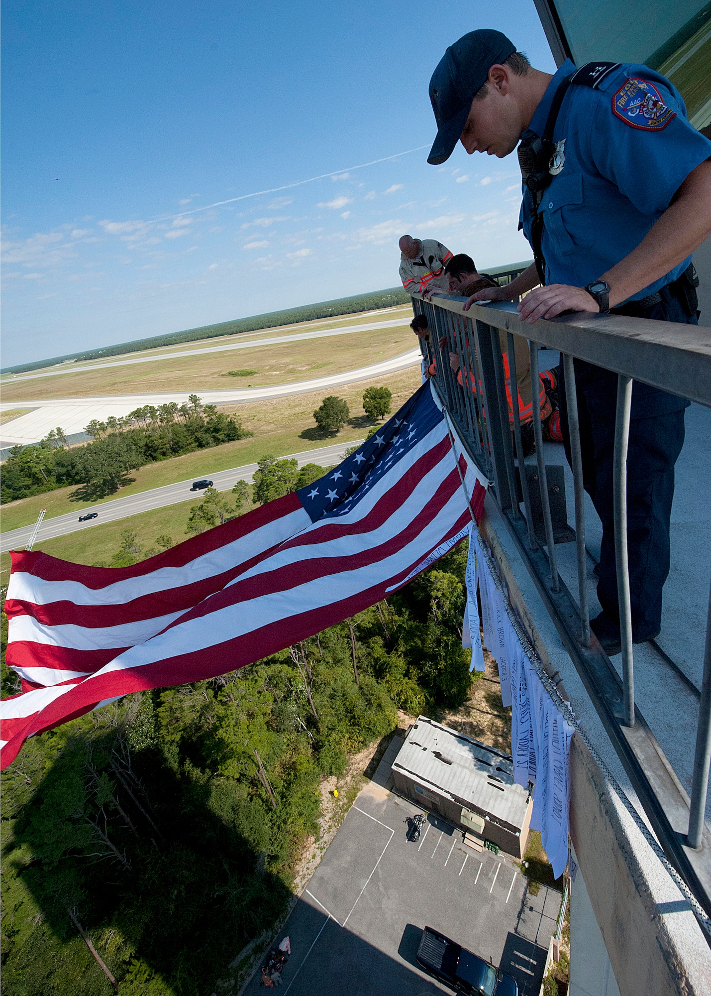 Mark Giuliano, the 96th Test Wing Fire Chief (background), coordinates the positioning of ribbons over the balcony. Fire department civilians and Airmen, ascended 11 stories carrying ribbons with the names of the 343 firefighters killed Sept. 11, 2001. The event ended on top of the tower with participants hanging the ribbons over the balcony on either side of the American Flag. (U.S. Air Force photo/Randy Gon)