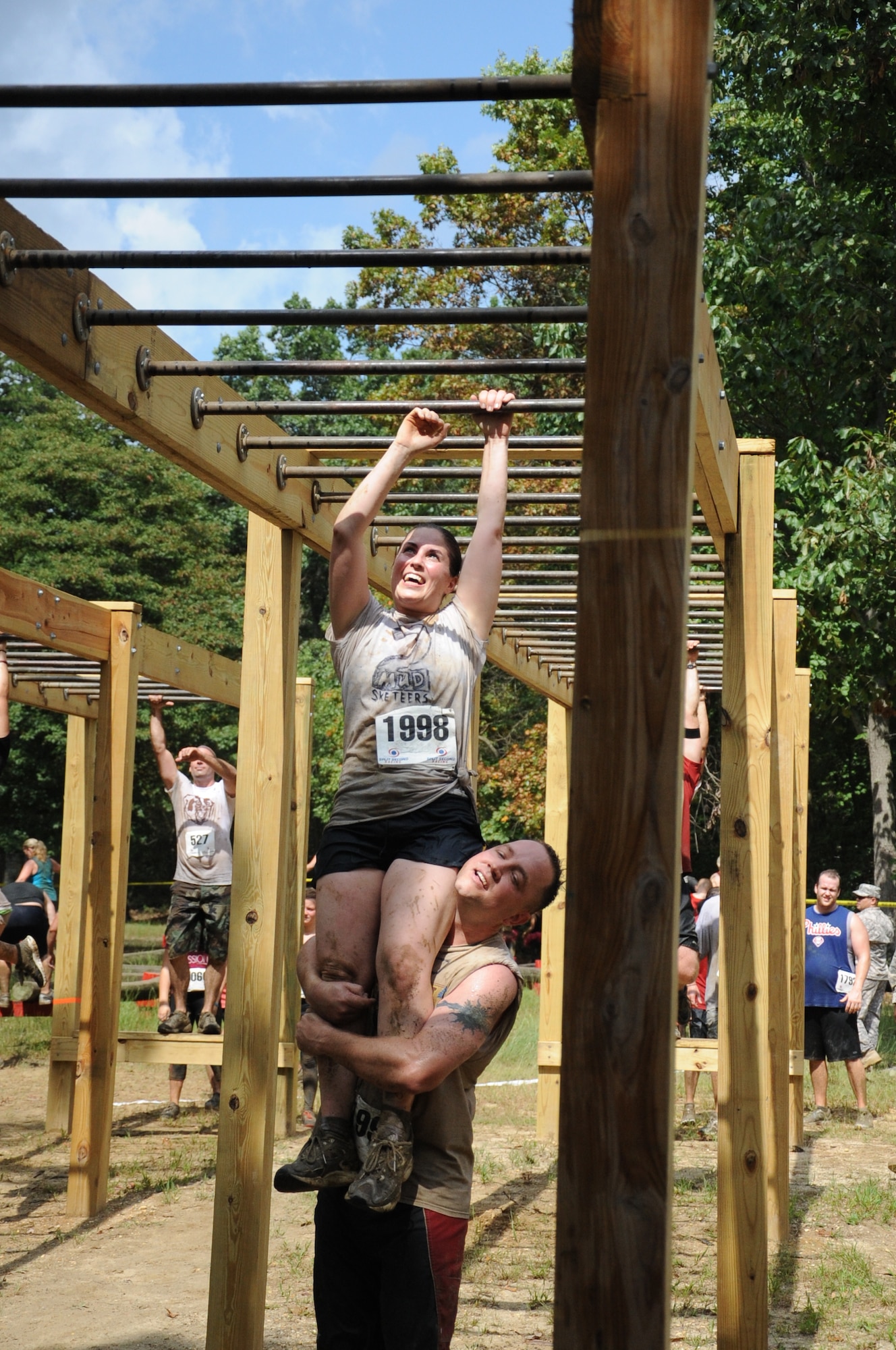 A mud run participant hoists a fellow runner on his shoulders to help her tackle the monkey bars Sept. 8 here. The monkey bars were part of the “Be All You Can Be” obstacle course the participants attempted as part of the Fifth Annual ‘Beast of the East’ Mud Run. (U.S. Air Force photo by 2nd Lt. Alexis McGee/Released)