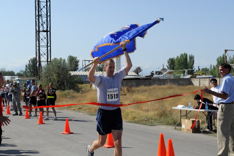 Col. Corey Martin crosses the finish line carrying the Air Force flag during the U.S. Air Force Marathon at the Transit Center at Manas, Kyrgyzsatan, Sept. 15, 2012. Over 150 participants took part in one of three categories; 10K, half marathon and a 26.2 mile marathon.  Martin serves as the 376th Air Expeditionary Wing commander and was the first to finish the full marathon with a time of 3:28:08. (U.S. Air Force photo/Master Sgt. Jason Vaught)