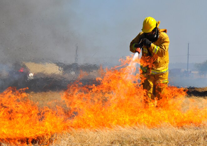 A U.S. Air Force firefighter extinguishes flames from a grass fire at Beale Air Force Base, Calif., Sept. 13, 2012. Beale firemen wear protective suites to shield them from heat. (U.S. Air Force photo by Staff Sgt. Robert M. Trujillo/Released)
