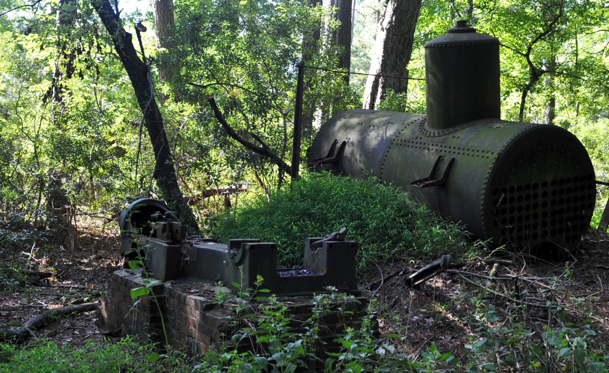 Remains of a steam engine (left) and a boiler from the Davis and Kimpton Brickyard rest in the woods at Training Area #23 on Fort Eustis, Va., Sept. 14, 2012. The brickyard, which operated from 1898 to the early 1900's, used these machines to power a series of lines and pulleys, which automated much of the brick-making process. (U.S. Air Force photo by Staff Sgt. Wesley Farnsworth / Released)