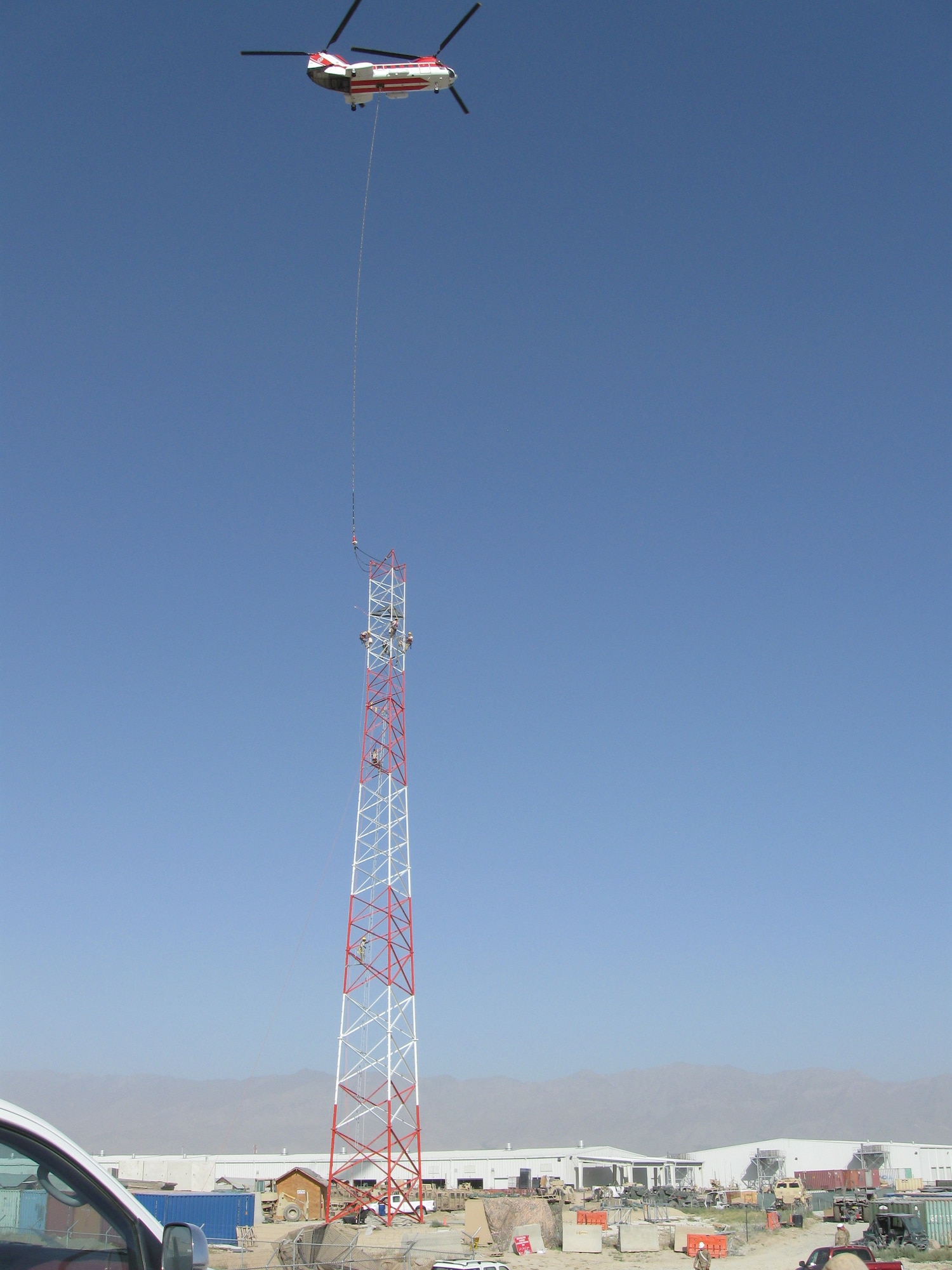 Members of 455th Expeditionary Communications Squadron assemble and connect tower sections as a civilian contractor helicopter and a high-reach crane lower sections into place. A specialized team from several Air National Guard Engineering Installation Squadrons deployed to Bagram Airfield, Afghanistan, combined their efforts to built and setup the 170-foot communications tower, greatly increasing radio communication range. (U.S. Air Force photo/1Lt. Bruce Champion)