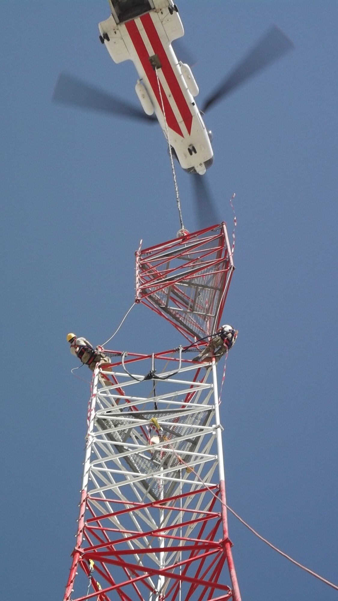 Members of 455th Expeditionary Communications Squadron prepare to connect tower sections when a civilian contractor helicopter lowers sections into place. A specialized team from several Air National Guard Engineering Installation Squadrons deployed to Bagram Airfield, Afghanistan, combined their efforts to built and setup the 170-foot communications tower, greatly increasing radio communication range. (U.S. Air Force photo/1Lt. Bruce Champion)