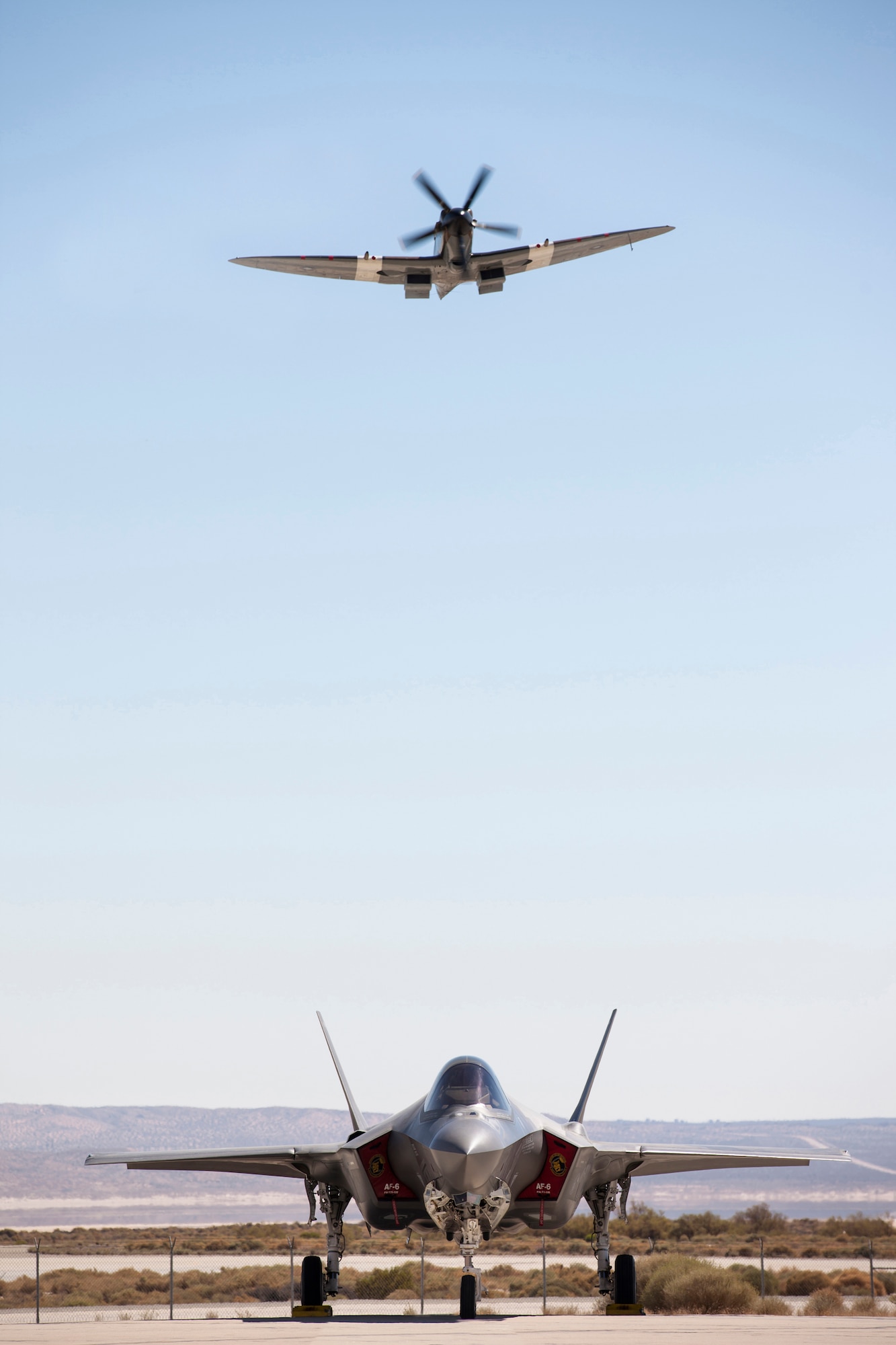 A World War II era Royal Air Force Spitfire flies over an F-35 Lightning II parked on the Edwards flightline.  The RAF fighter was brought in Sept. 14 to celebrate "Battle of Britain Night" hosted by the United Kingdom Lightning II Test and Evaluation Squadron. (Photo by Matthew Short/Lockheed Martin)