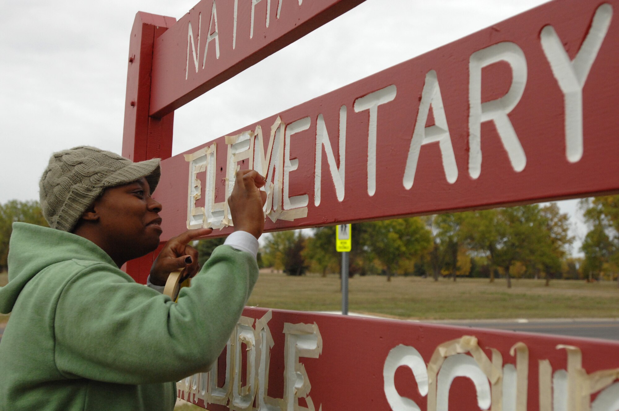 CeeCee Long, a Grand Forks Air Force Base parent, removes tape from the Nathan Twining Elementary and Middle School sign after applying a fresh coat of paint to the lettering as part of Twining and Eielson’s Fall Beautification Day. Other volunteers performed tasks such as gardening, raking dead grass and leaves, and edging sidewalks. (U.S. Air Force photo/Senior Airman Susan L. Davis)