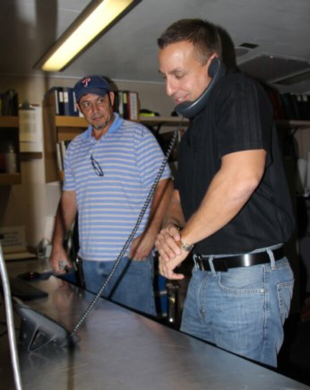 Greg Formosa (right) makes a VoIP (Voice over Internet Protocol) phone call aboard the US Dredge Wheeler as Tim Stirling looks on.