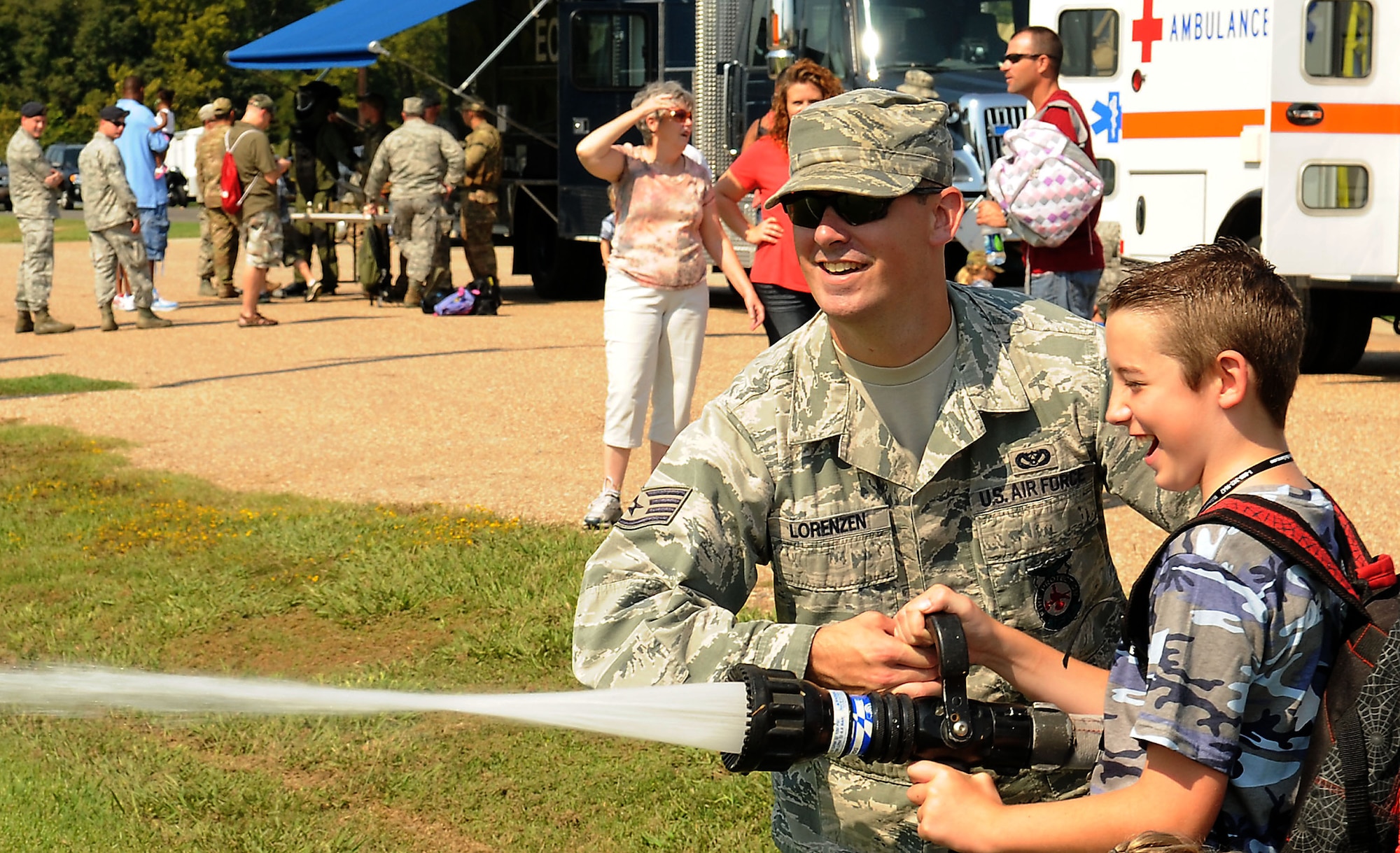 Staff Sgt. Jordan Lorenzen, 2nd Civil Engineer Squadron crew chief, assists Tyler Snyder, 11, son of Master Sgt. Michael Snyder, 2nd Logistics Readiness Squadron, to spray a fire hose during Operation Hero on Barksdale Air Force Base, La., Sept. 22. The annual event is a child-friendly personnel deployment line and features a number of activities for kids throughout the day, including a weapons qualification course with paintball guns, face-painting and a physical fitness assessment. (U.S. Air Force photo/Senior Airman Kristin High)(RELEASED)
