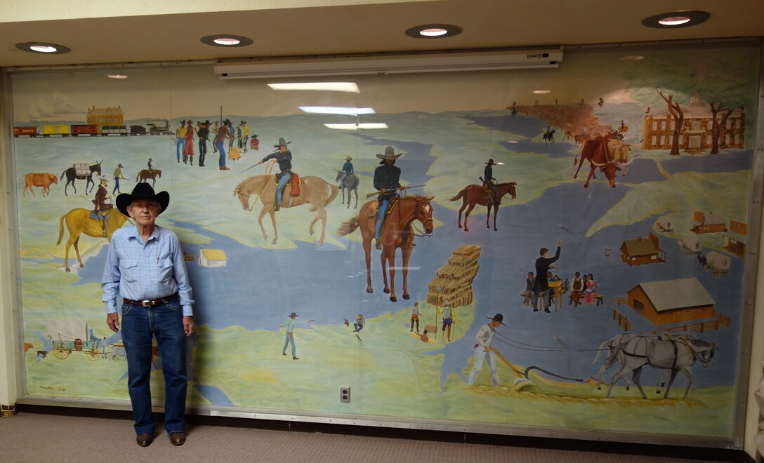Monroe Moore poses with the mural he painted in 1968 in the Eufaula Powerhouse lobby. 
