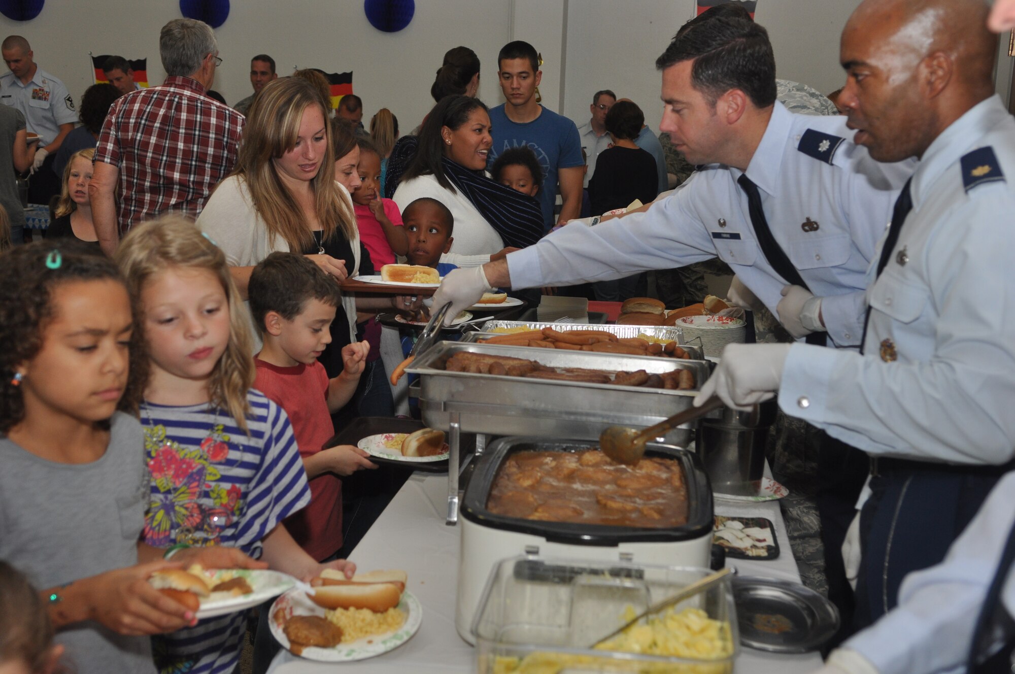 Maj. Fernando Waldron, 62nd Airlift Wing comptroller and Lt. Col. Robert Farkas, 62nd Aerial Port Squadron commander, serve meals to families of deployed Airmen during the quarterly deployed families dinner at the McChord Field Chapel Support Center, Sept. 24, 2012 at Joint Base Lewis-McChord, Wash. The theme for this quarters event was German food. (U.S. Air Force photo/Staff Sgt. Sean Tobin)