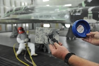 John Harris, 12th Flying Training Wing Maintenance Division media blast technician, holds sample items made from recycled media blast material as John Esquivel (left) uses corn starch to strip the paint from a T-38 Talon at Joint Base San Antonio-Randolph, Sept. 20. Two materials 12th FTW shops air blast to remove paint from T-1, T-6, T-38 and F-16 aircraft are plastic and corn starch, which have been deemed environmentally safe by the Air Force.
Randolph generates about 20,000 pounds of plastic and 28,500 pounds of corn starch annually that is recycled.  The excess plastic is shipped to Canton, Ohio, where it is manufactured into products such as simulated marble tiles and dog bowls.  (U.S. Air Force photo by Rich McFadden) 