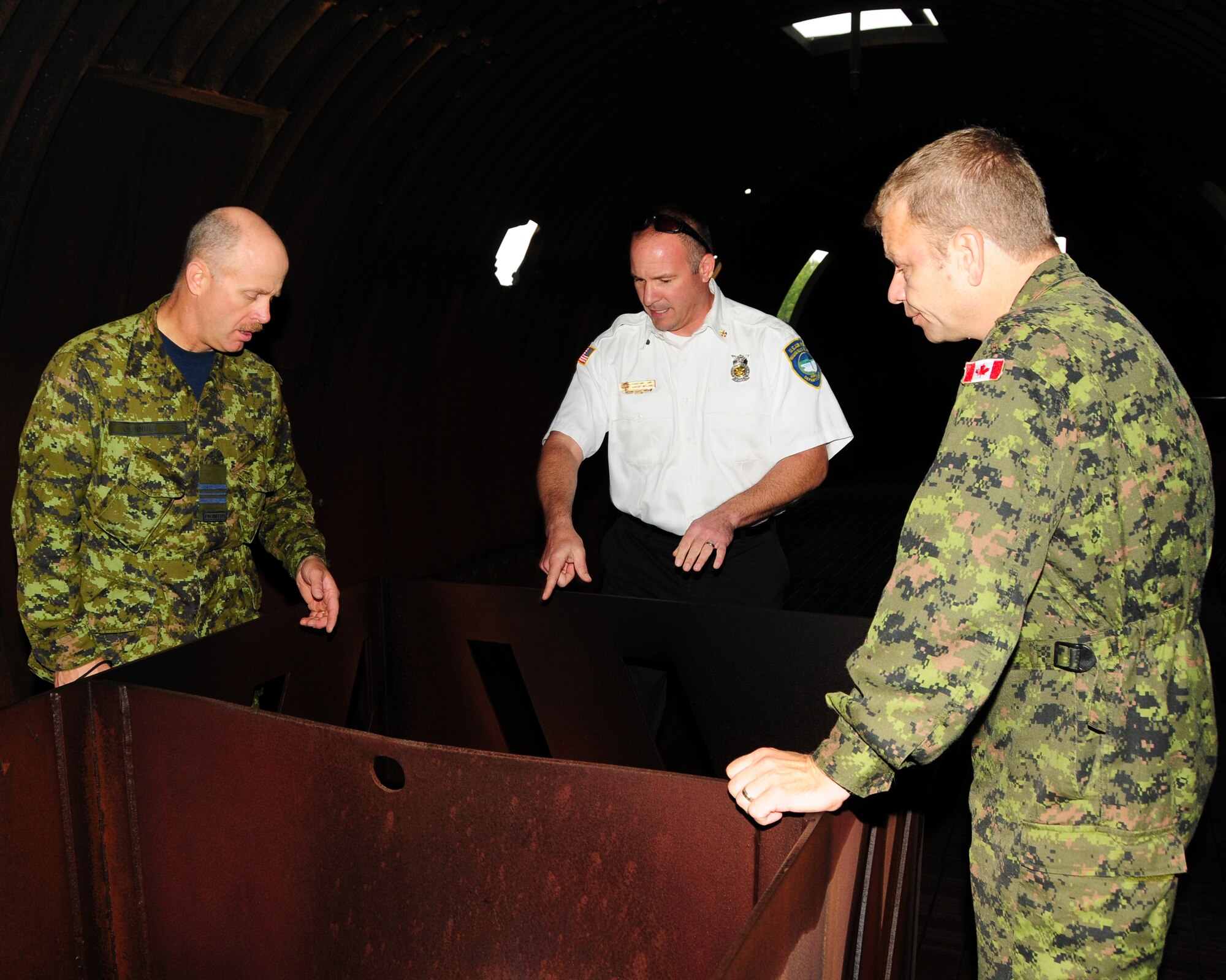 Assistant Fire Chief Aaron McLane (center), Niagara Falls Air Reserve Station Fire Emergency Services, explains how the propane gas is ignited when using the aircraft fire training simulator to Major Rick Dunning (left), 1 Canadian Air Division Fire Marshall for the Royal Canadian Air Force and Warrant Officer Ron Johnson, 8 Wing Canadian Forces Base Trenton, Platoon Fire Chief on September 26, 2012 at the Niagara Falls Air Reserve Station, N.Y.  The Canadians were here to do a comparative analysis between what the U.S. Air Force is using to train their firefighters compared to what Canadian Forces have. (U.S. Air Force photo by Peter Borys)