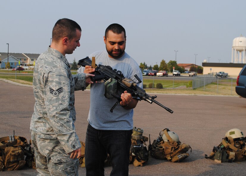 Senior Airman Thomas Browne, 341st Security Forces Group Tactical Response Force member, shows Salvador Gonzalez an automatic rifle at the T-9 trainer. Former U.S. Marine Corps heavy machine gun operator and wounded veteran, Gonzalez had a chance to interact with 341st SFG Airmen during the “Never Quit Series” Gunner Tour and share his experiences from being in Iraq. (U.S. Air Force photo/Airman 1st Class Katrina Heikkinen)