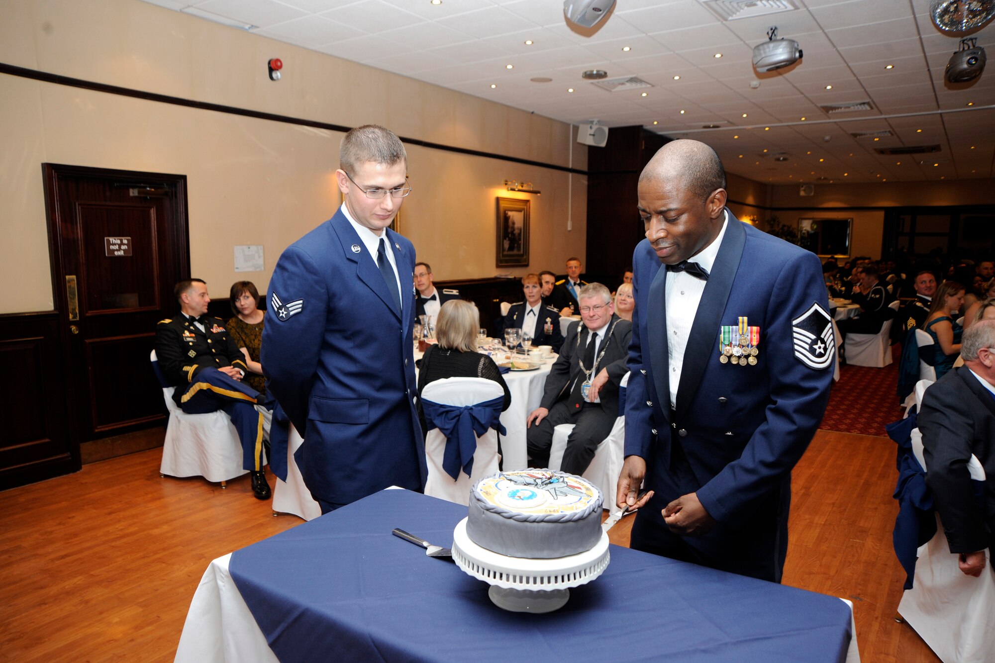 RAF MENWITH HILL, United Kingdom - Master Sgt. Darnell Adams (right), 421st Medical Flight, and Senior Airman Shelby Woodrum, 451st Intelligence Squadron, make the first ceremonial cuts in the Air Force Ball cake at the RAF Menwith Hill Community Club Sept. 21. This year’s guest speaker was Brig. Gen. John Bansemer, Director of Intelligence, Headquarters U.S. European Command. (U.S. Air Force photo by Staff Sgt. Brok McCarthy)