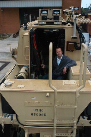 Naval Surface Warfare Center Panama City Buffalo Systems Deputy Project Engineer Steven “Tate” Carow sits near the rear-door assist mechanism. The RDA is an upgrade developed to push and hold open the rear door aboard the Marine Corps Buffalo Mine Resistant Ambush Protected vehicle. For Carow and his team, completion of this particular capability insertion helps to fulfill a critical requirement to improve crew survivability. The design uses a ruggedized motor controller, which activates a linear actuator and hydraulic cylinder. 