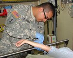 Spc. Manuel Chavarria (left) starts an IV on a patient in the Emergency Department of the Christus Spohn Memorial Hospital staff. The Texas National Guardsman trains in the civilian hospital during their drill weekends.