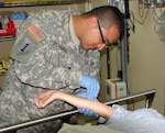 Spc. Manuel Chavarria (left) starts an IV on a patient in the Emergency Department of the Christus Spohn Memorial Hospital staff. The Texas National Guardsman trains in the civilian hospital during their drill weekends.