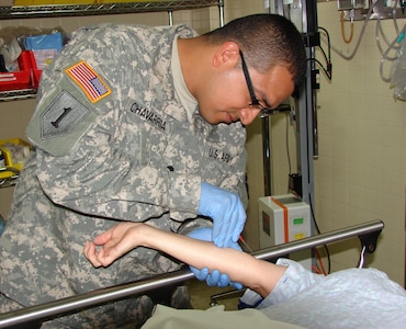 Spc. Manuel Chavarria (left) starts an IV on a patient in the Emergency Department of the Christus Spohn Memorial Hospital staff. The Texas National Guardsman trains in the civilian hospital during their drill weekends.