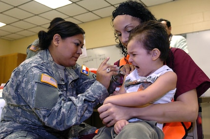 Texas Army National Guard Spc. Stephanie Cardenas, an Emergency Medical Technician for Joint Forces Headquarters of San Antonio, gives a vaccination shot to four-year-old Jeremiah Burkett while he is comforted by his mother. The boy will be ready for pre-kindergarten this fall, at least as far as immunizations go, thanks to the free vaccinations offered in Brownsville during Operation Lone Star.