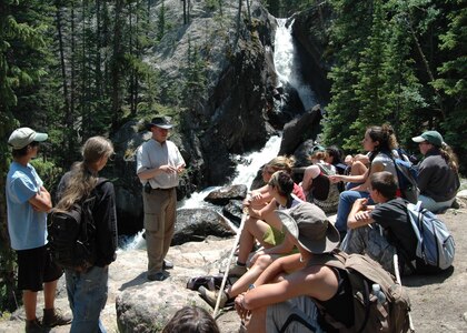 Campers listen intently to Air Guard Staff Sgt. David Fort as he teaches them about survival techniques after Fort led them on a two mile hike in the Roosevelt Forest in Colorado July 10, 2007. The youth had lunch on a cliff overlooking a waterfall before heading back to camp.