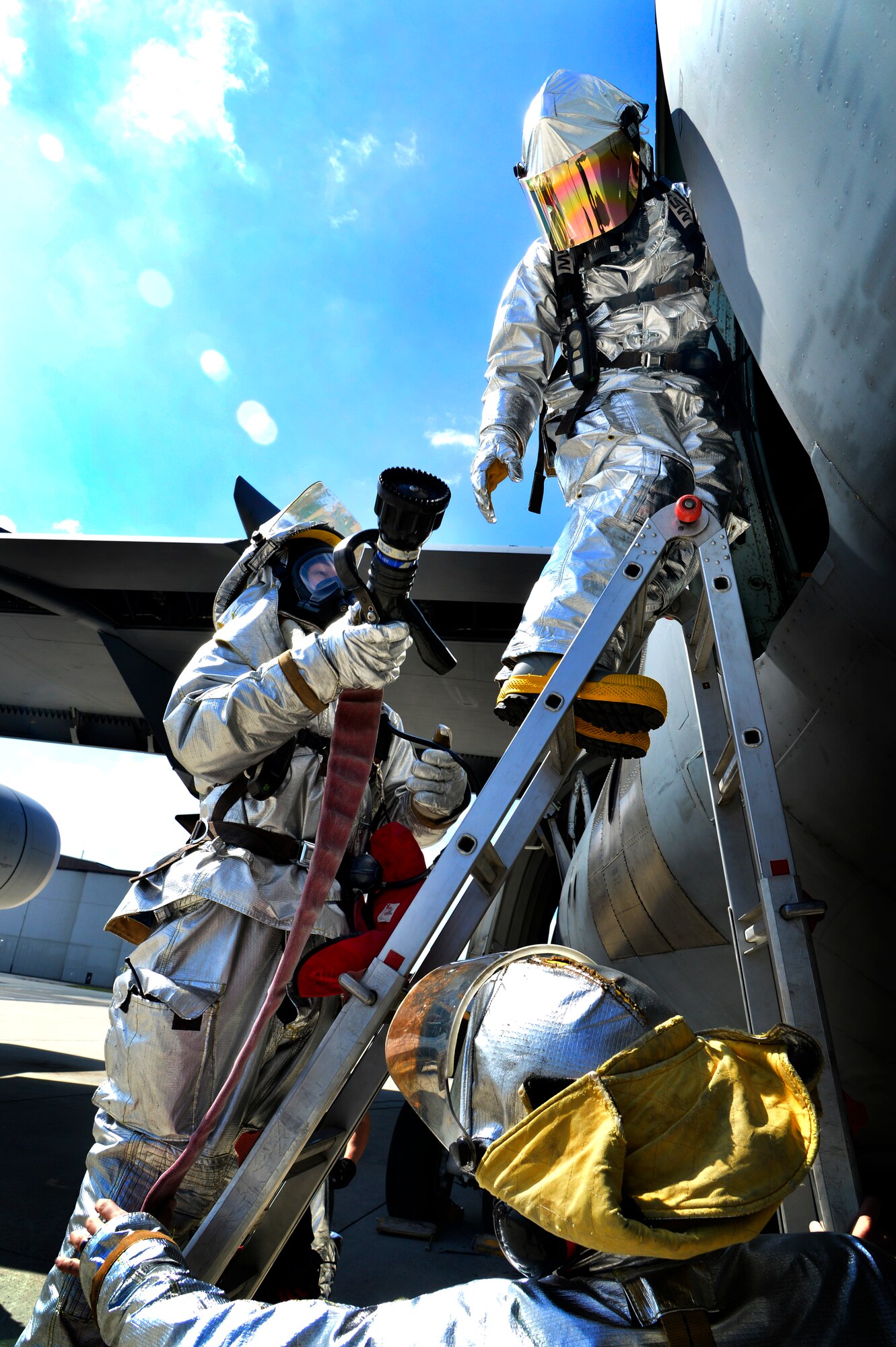 A member of the 436th Civil Engineer Squadron fire department hands a fire hose to another firefighter while another holds the ladder March 29, 2013, at Dover Air Force Base, Del. The fire department practiced emergency aircrew retrieval techniques and firefighting. (U.S. Air Force photo/David Tucker)