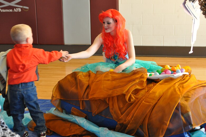 Kelsie Inman, playing a little mermaid, hands Easter eggs to a child March 30, at the RP Lee Youth Center as part of the Easter Egg-Stravaganza. The event, hosted by the 21st Force Support Squadron, featured the Kia Hamstars, arts and crafts by Tierra Vista Communities, and a little mermaid theme. (U.S. Air Force photo/Margaret Arnold)
