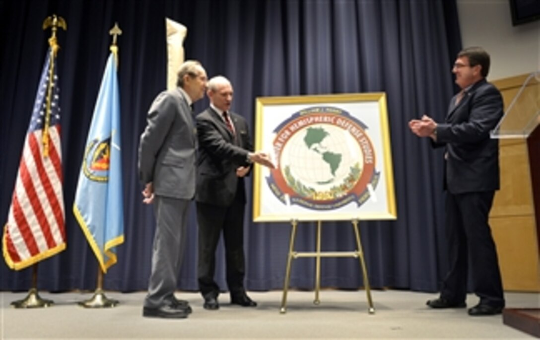 The 19th Secretary of Defense William J. Perry, left, listens as Kenneth A. LaPlante, second from left, presents the logo of the newly renamed William J. Perry Center for Hemispheric Defense Studies at the National Defense University at Fort McNair in Washington, D.C., on April 2, 2013.  Deputy Secretary of Defense Ashton B. Carter, right, joined LaPlante in honoring Perry at the ceremony.  LaPlante is the acting director of the Center.  