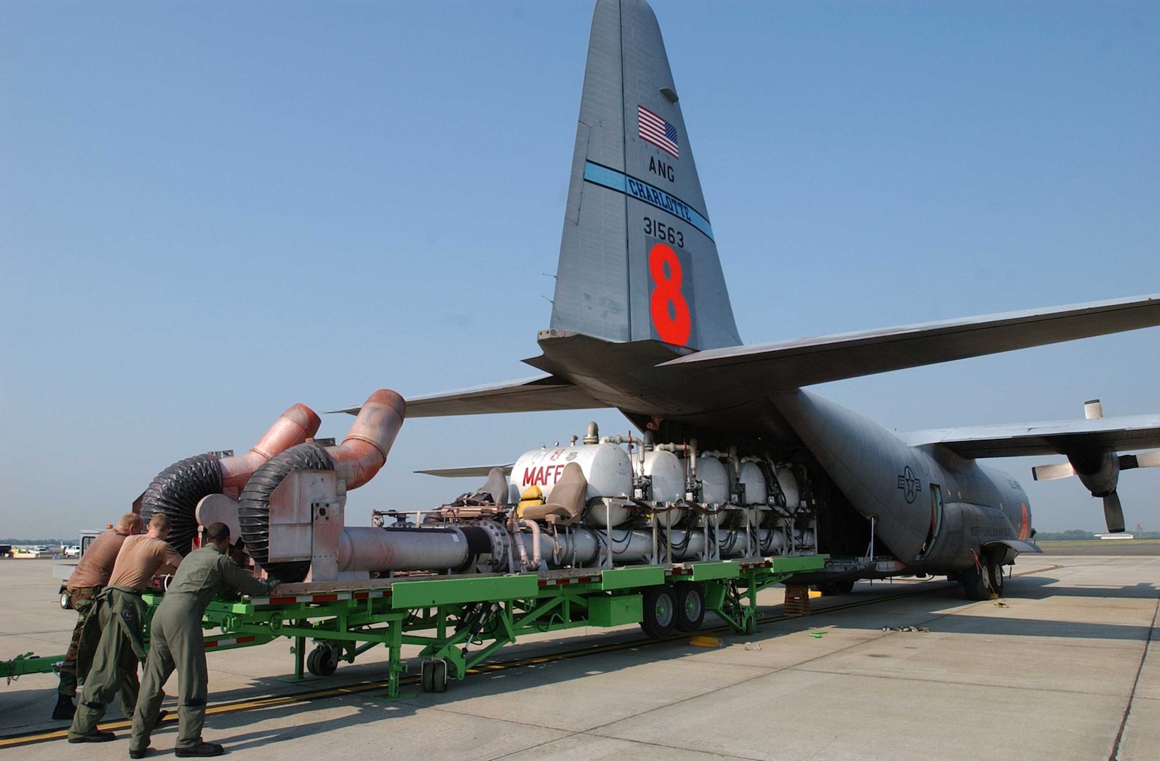 Airmen from the North Carolina Air National Guard's 145th Airlift Wing push a modular airborne fire fighting system onto a C-130 Hercules. The system is a series of pressurized tanks that hold 3,000 gallons of flame-retardant liquid. The retardant is dropped along the leading edge of a fire to block the spread of flames.