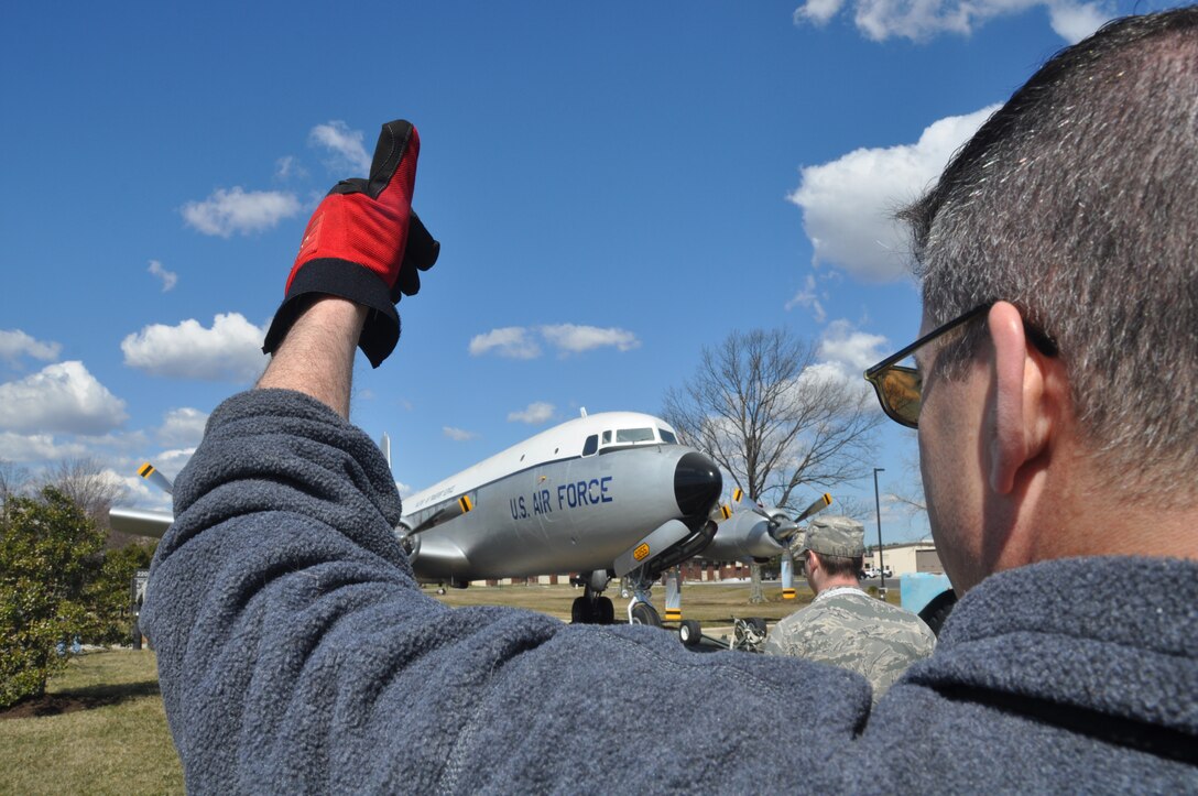 JOINT BASE MCGUIRE-DIX-LAKEHURST, N.J. - SMSgt. Christopher Hofrichter, project manager, signals the historic C-118 aircraft is clear from obstruction as volunteers from the 514th and 305th Air Mobility Wings and 87th Air Base Wing move the newly refurbished aircraft from the hangar to its static display location in front of the McGuire Passenger Terminal on March 23. (U.S. Air Force photo/Master Sgt. Donna T. Jeffries)