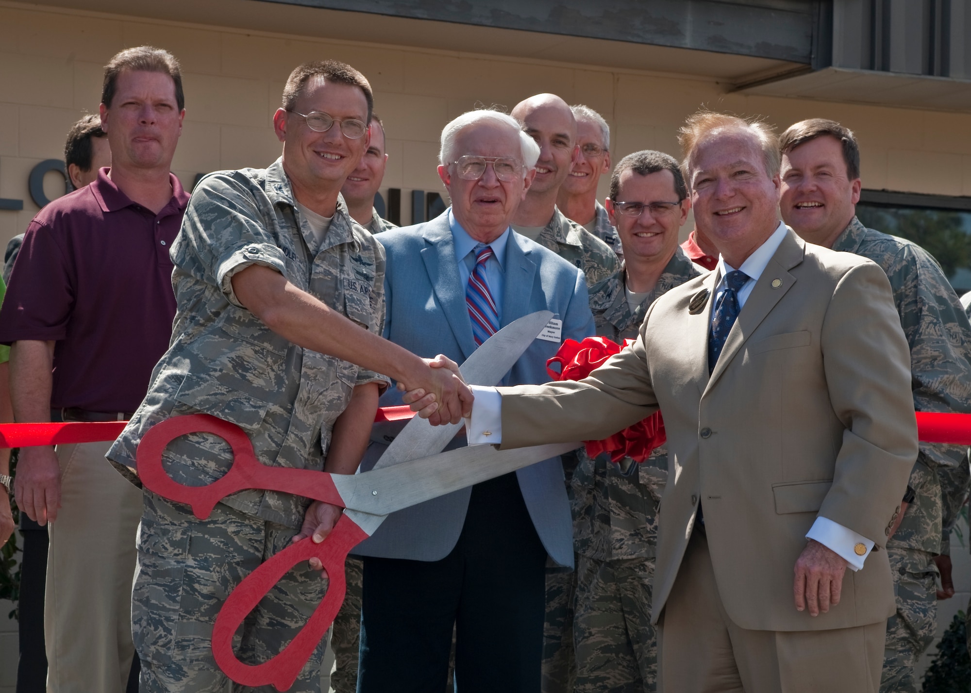 Col. Douglas Dudley, commander of 1st Special Operations Mission Support Group and Ben Anderson, Okaloosa County tax collector, shake hands and cut the grand opening ribbon in front of the building that houses the Okaloosa County Tax Collector office with many of the personnel that directly contributed the fruition of the project standing behind them.  Dudley spoke at the ribbon cutting ceremony, stating the convenience of having the office on base and the time saving benefits it would provide Team Hurlburt.  (U.S. Air Force Photo by Airman 1st Class Nigel Sandridge)   